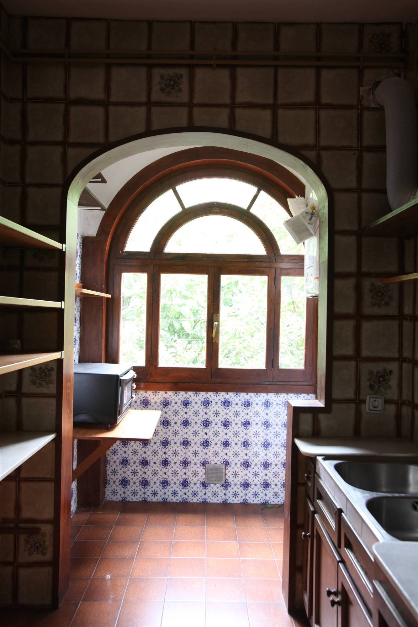 Cocina antigua con ventana de madera y azulejos pintados.