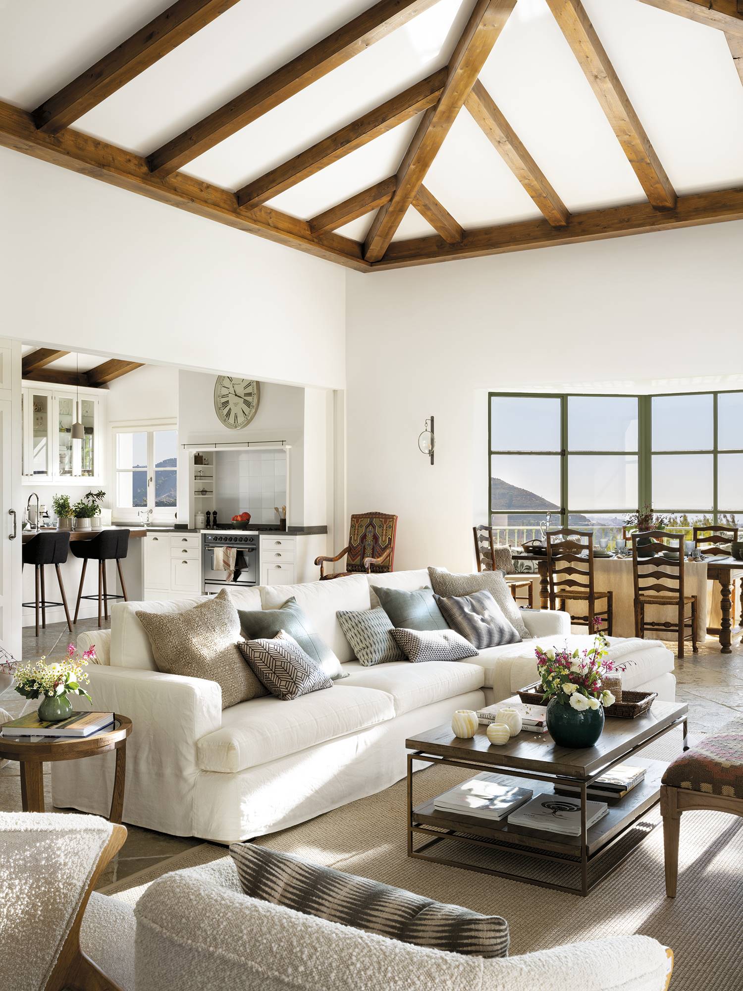 Salón con vigas de madera en el techo, sofá blanco, ventanal y mesa de centro de madera.