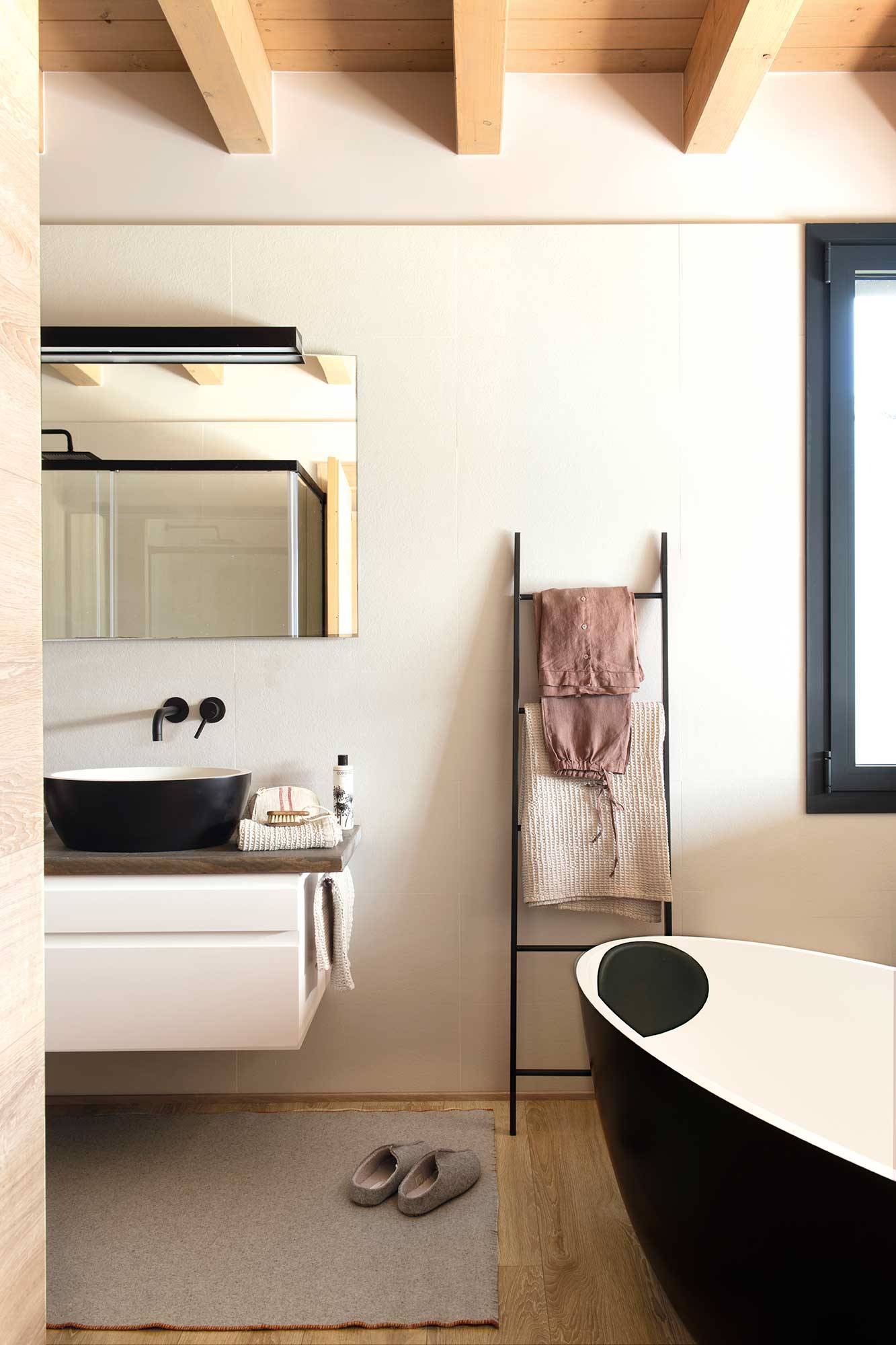 Baño rústico moderno con vigas de madera y bañera exenta negra. 