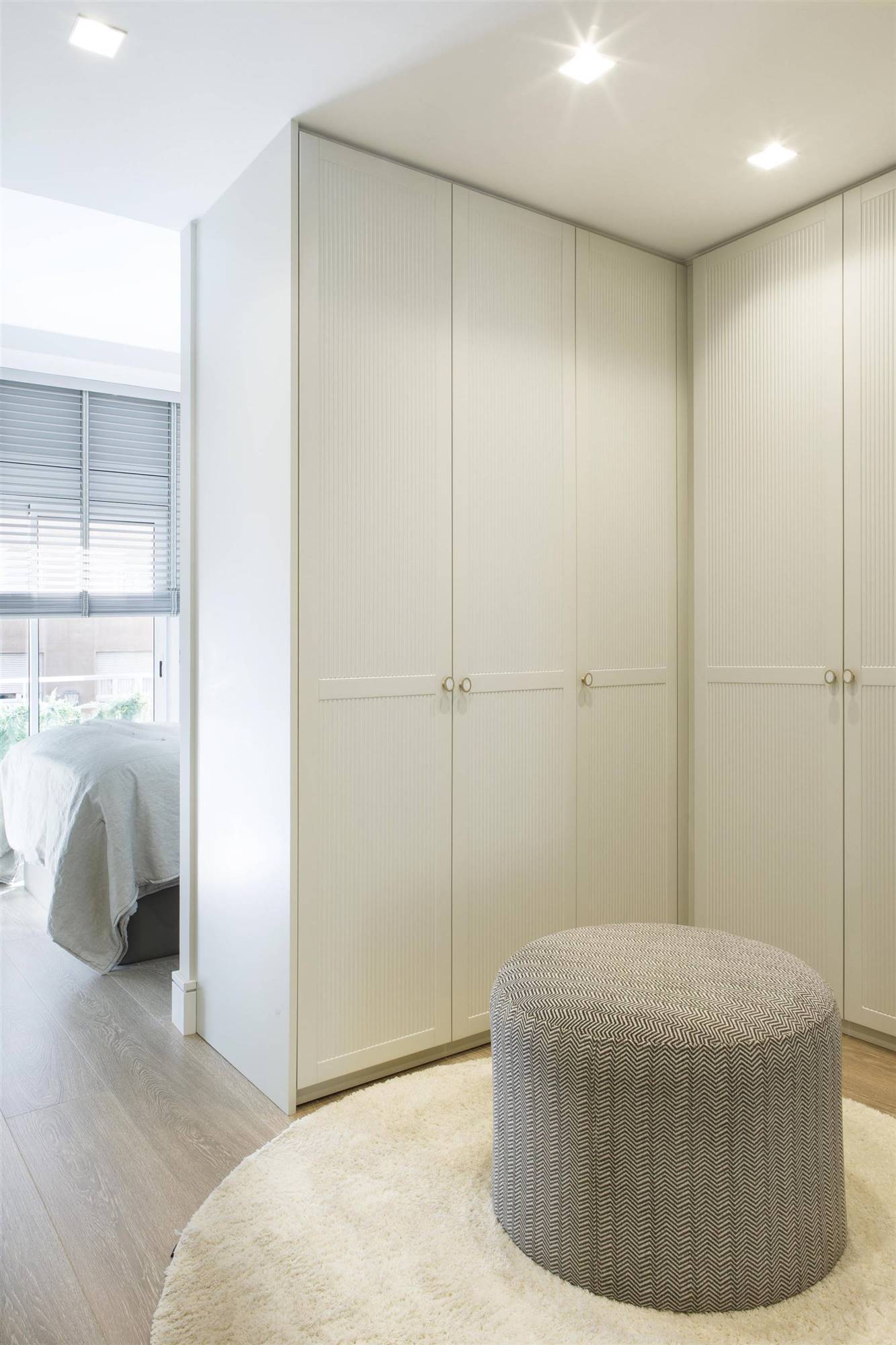 Vestidor con armarios blancos, alfombra y puf en habitación suite proyecto de Pia Capdevila.