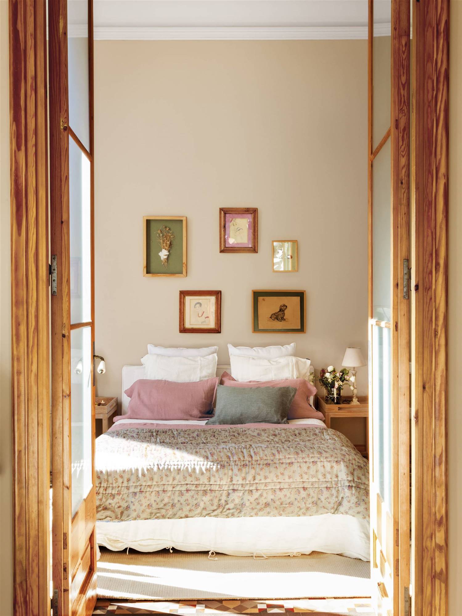 Dormitorio principal con cama, puertas de madera y cuadros encima del cabecero. 