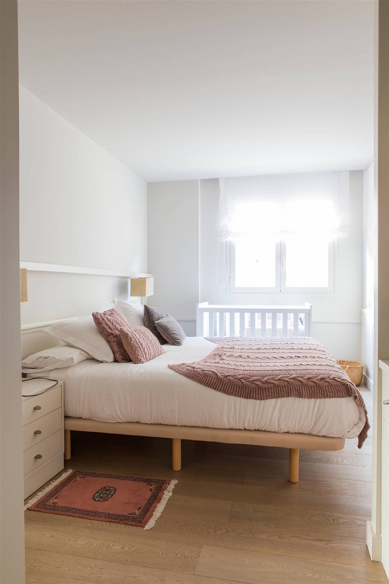 Dormitorio con cama alta y colcha en color rosa empolvado.