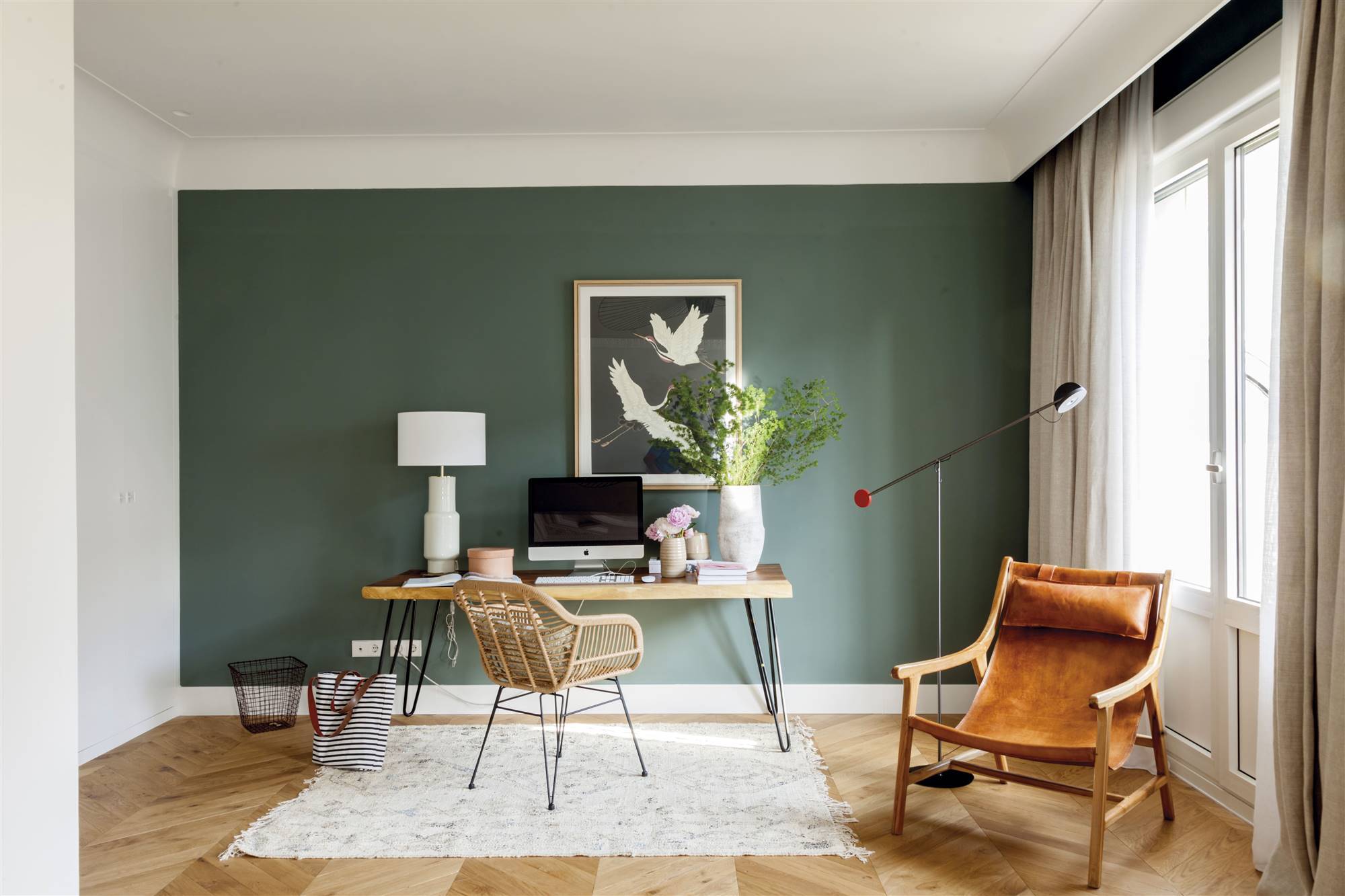 Despacho con escritorio y pared pintada en verde junto a zona de lectura con silla de cuero. 
