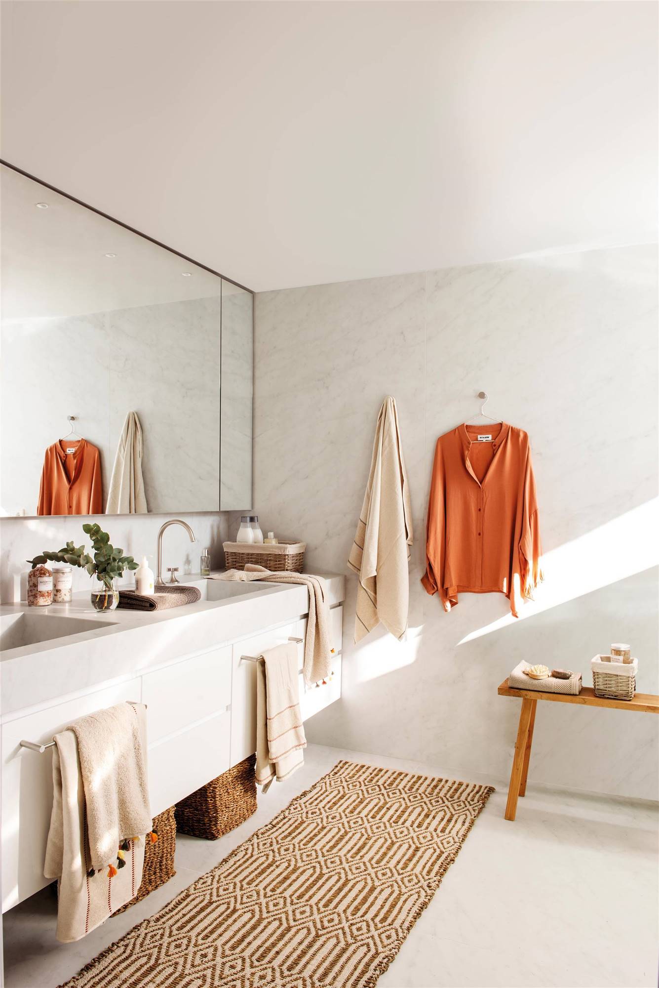 Baño decorado en blanco con alfombra vistosa en color mostaza y motivos geométricos.
