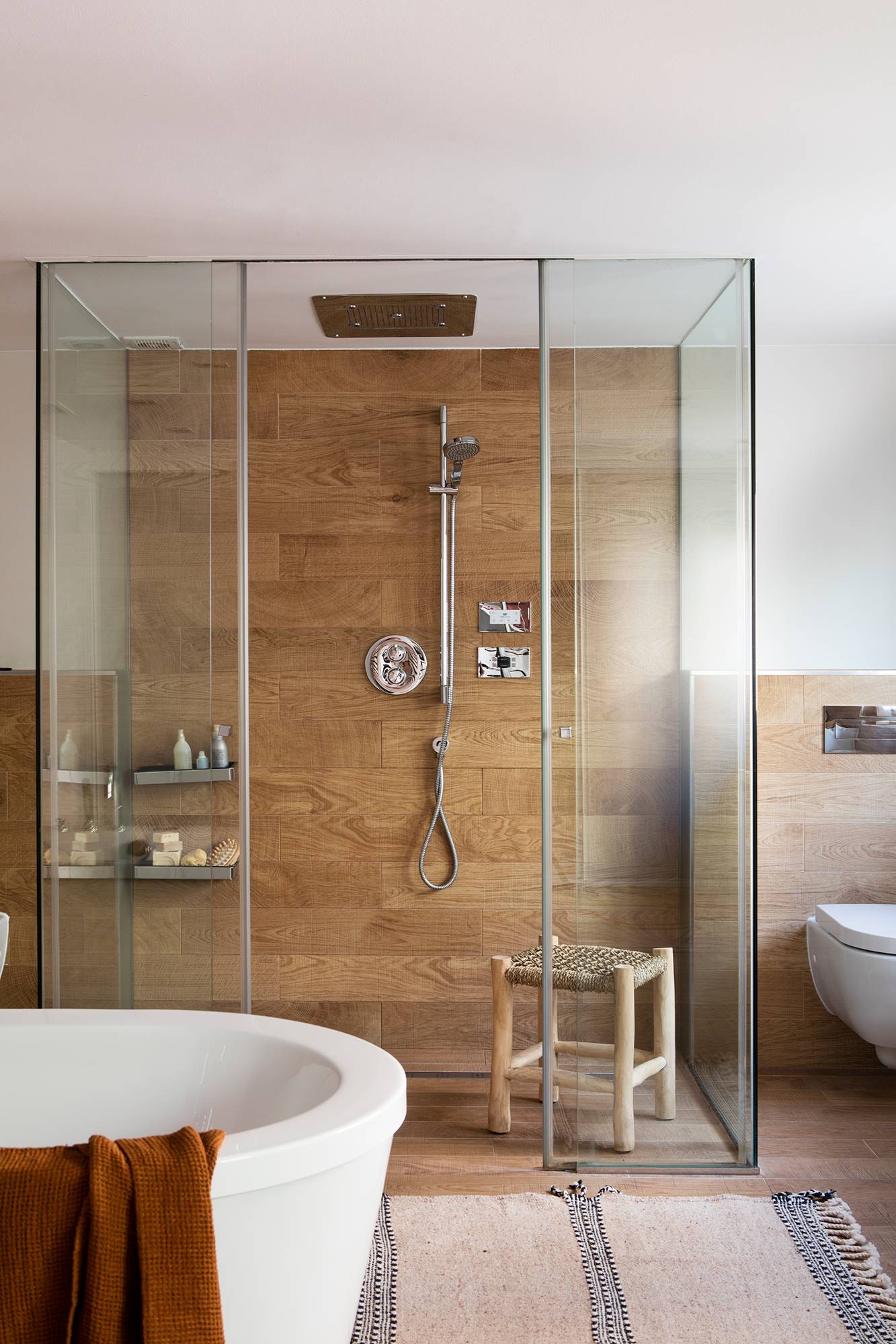 Baño con ducha blanca exenta ovalada, ducha revestida de madera y alfombra.