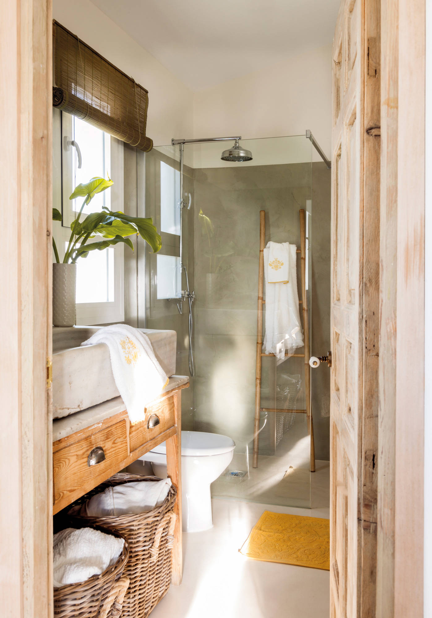 Baño pequeño con mueble recuperado de madera y ducha con mampara transparente.