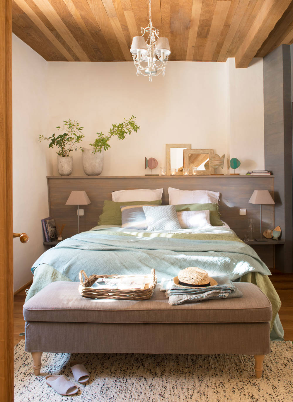 Dormitorio con banqueta, cama y techo de madera. 