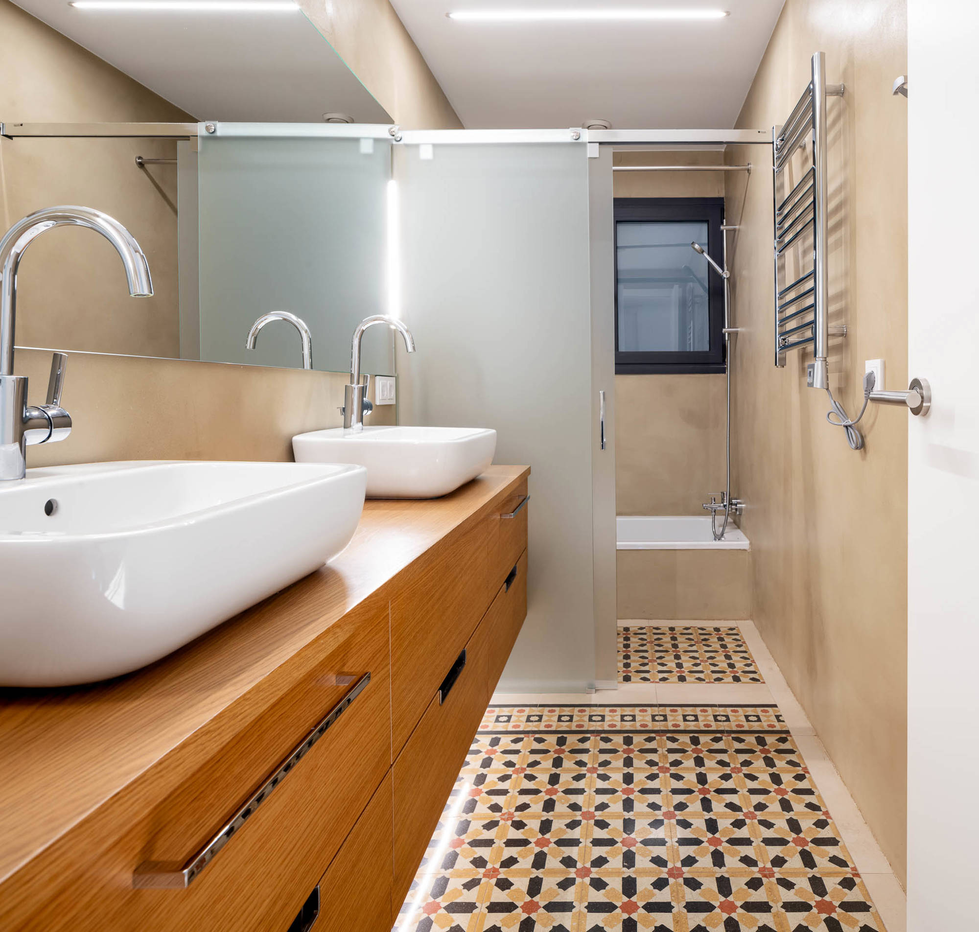 Baño después de la reforma con azulejos hidráulicos del siglo XX, bañera y mueble de madera con dos lavamanos. 