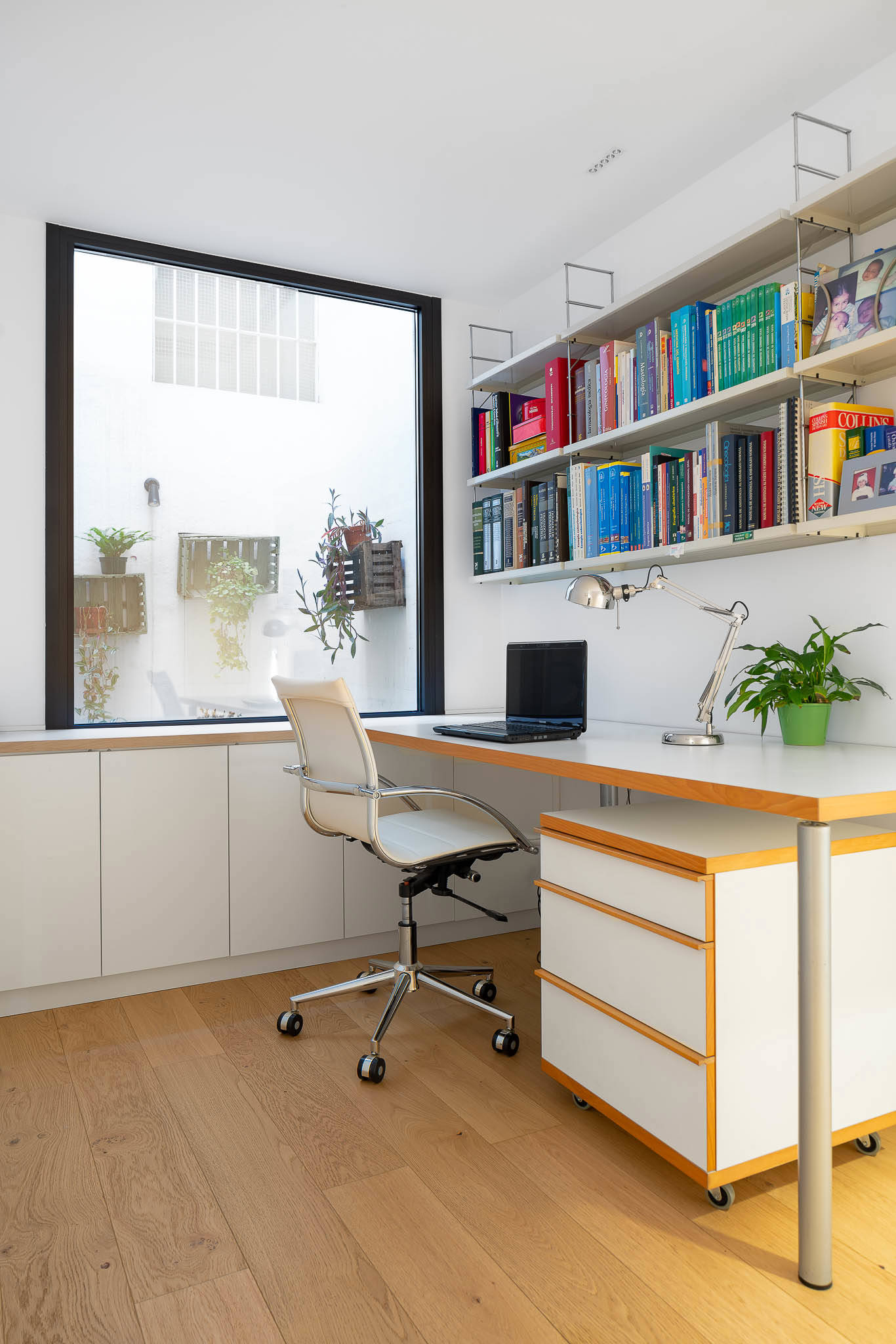 Despacho después de la reforma con suelo de madera, escritorio blanco con estantería y gran ventana. 