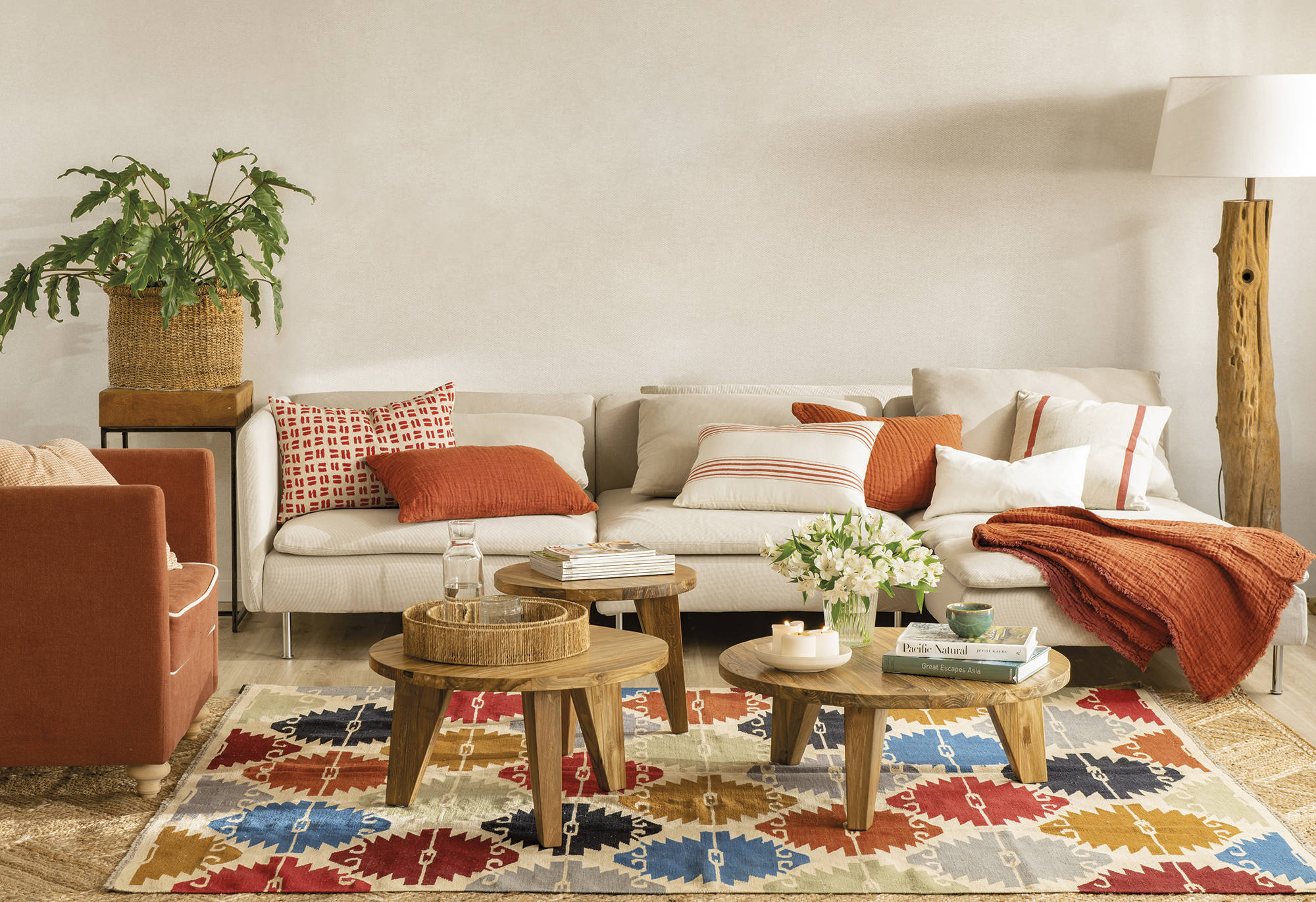 Salón con un sofá neutro con cojines y butaca en color teja y mesa de centro redondas