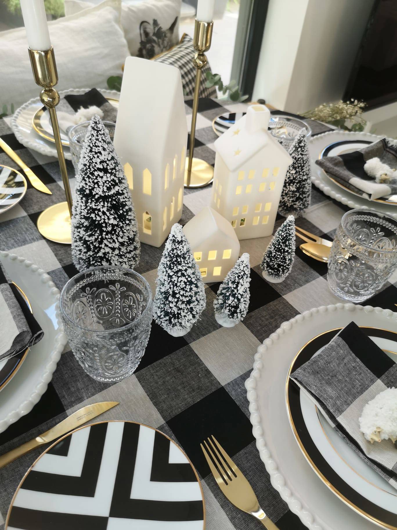 Comedor con mesa navideña con mantel de cuadros vichy, velas, vajilla, arbolitos decorativos y luces en forma de casitas de IKEA.