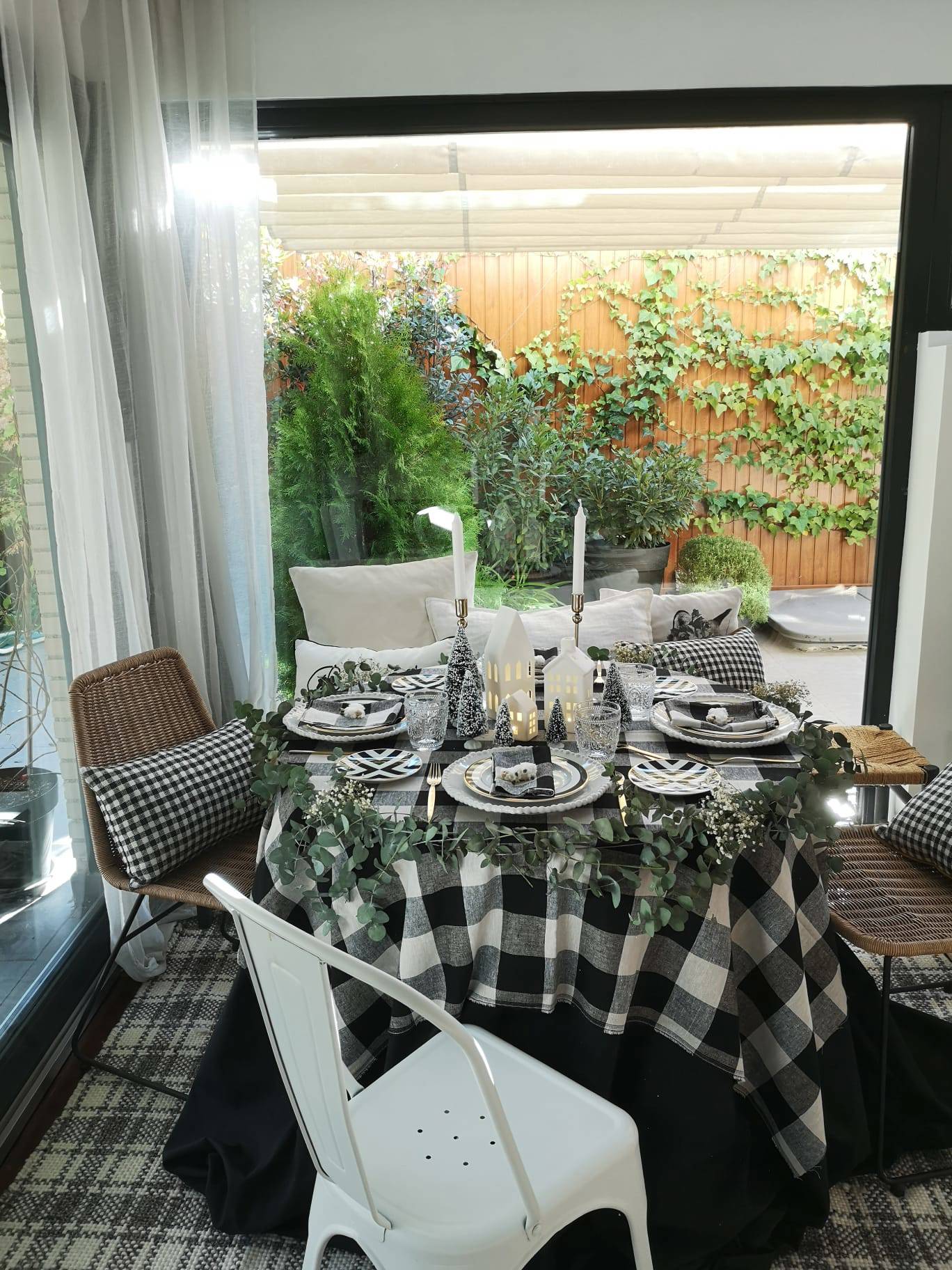 Comedor con mesa navideña con mantel de cuadros blanco y negro, sillas de fibras, banco con cojines y lámparas en forma de casita, de IKEA.