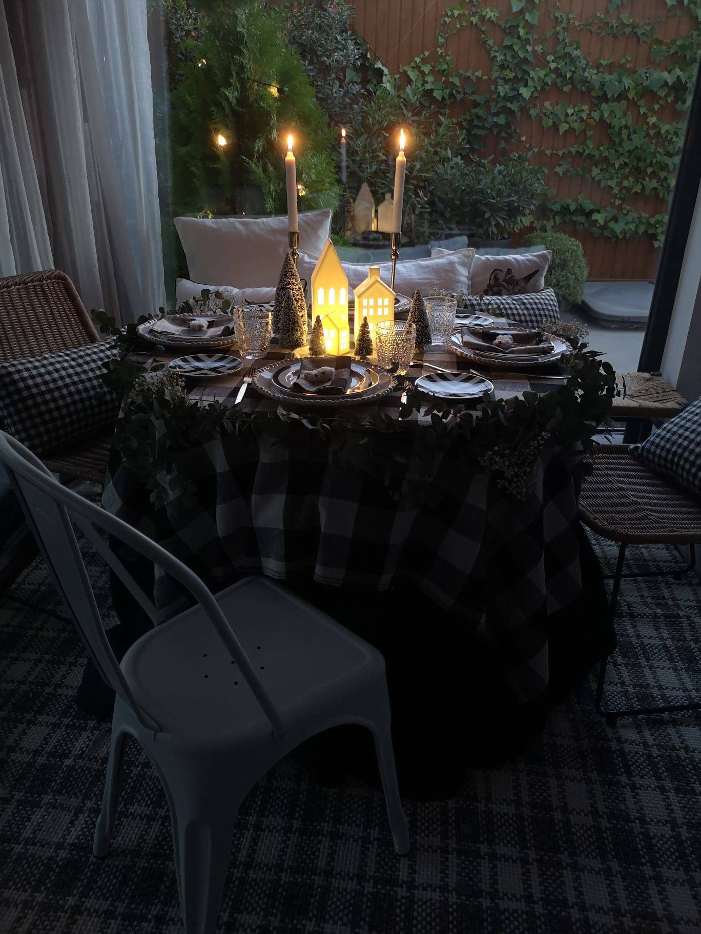Comedor de noche con mesa navideña con mantel de cuadro, velas y lámparas de mesa en forma de casita de IKEA.
