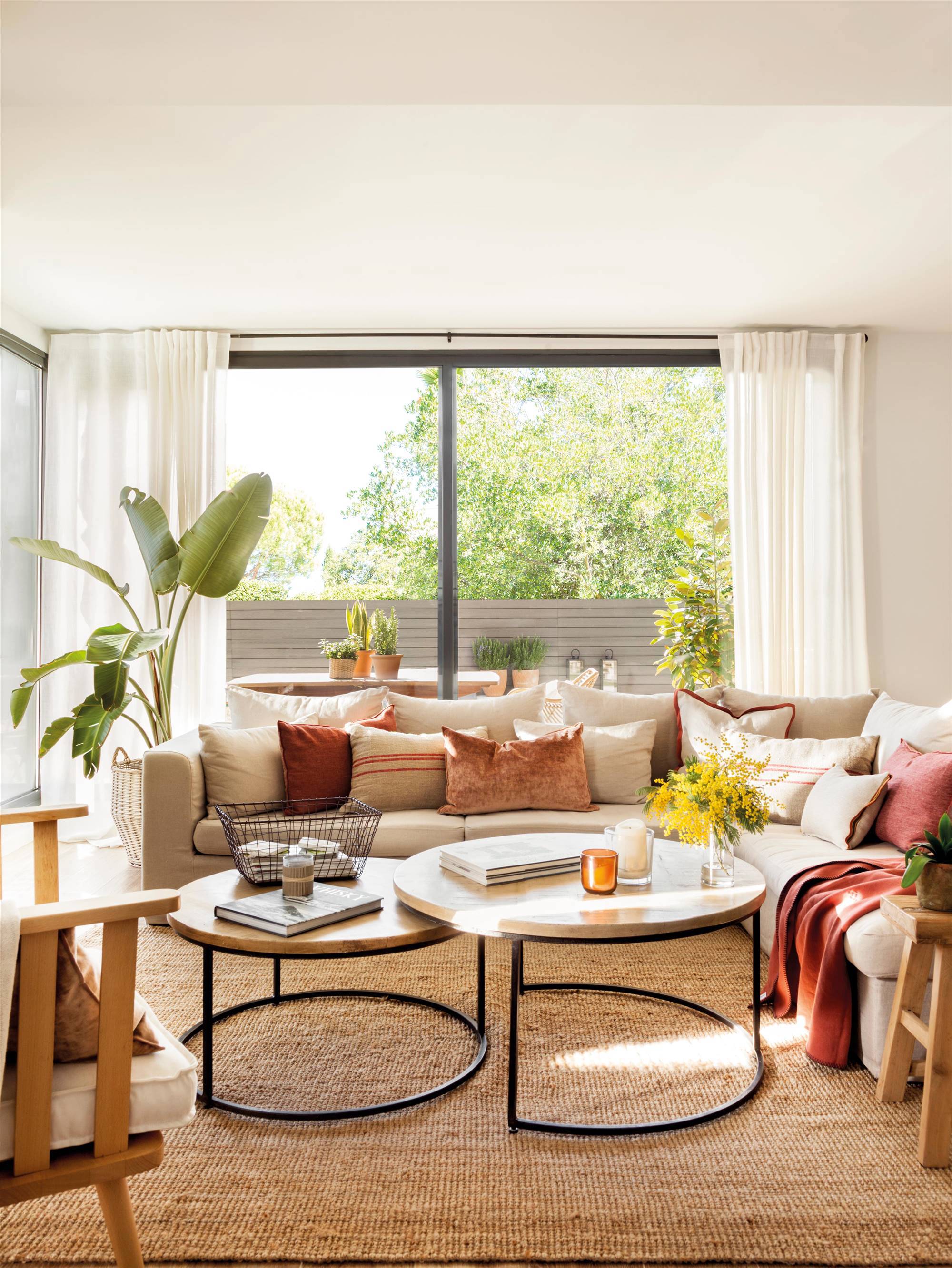 Salón con sofá en forma de L, mesas redondas tipo nido, terraza y plantas