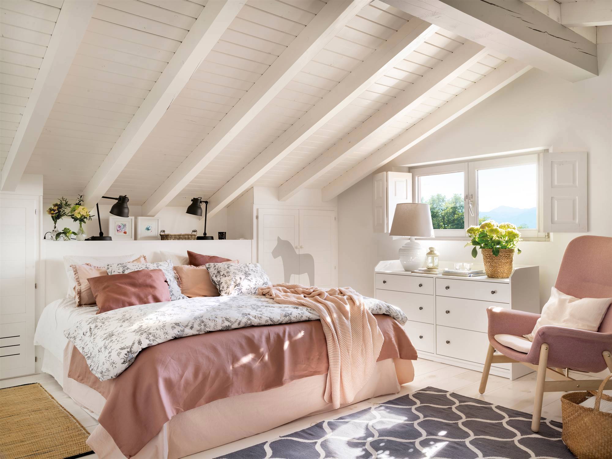 Dormitorio abuhardillado pintado en blanco con butaca rosa.