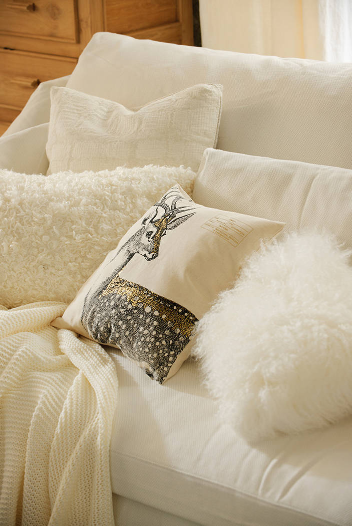 Sofá blanco con cojines de pelo y estampado con figura de reno.