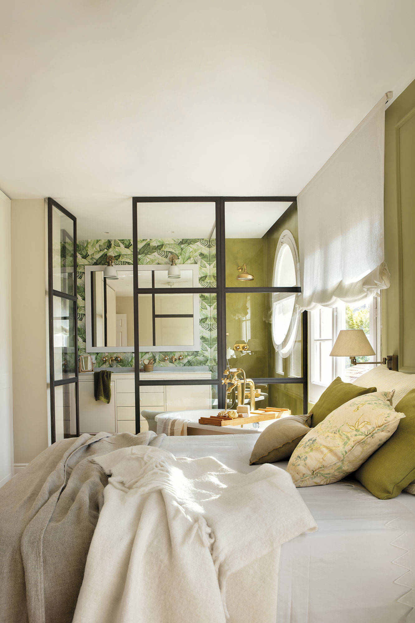 Dormitorio verde con pared de cristal que separa el baño de la habitación.