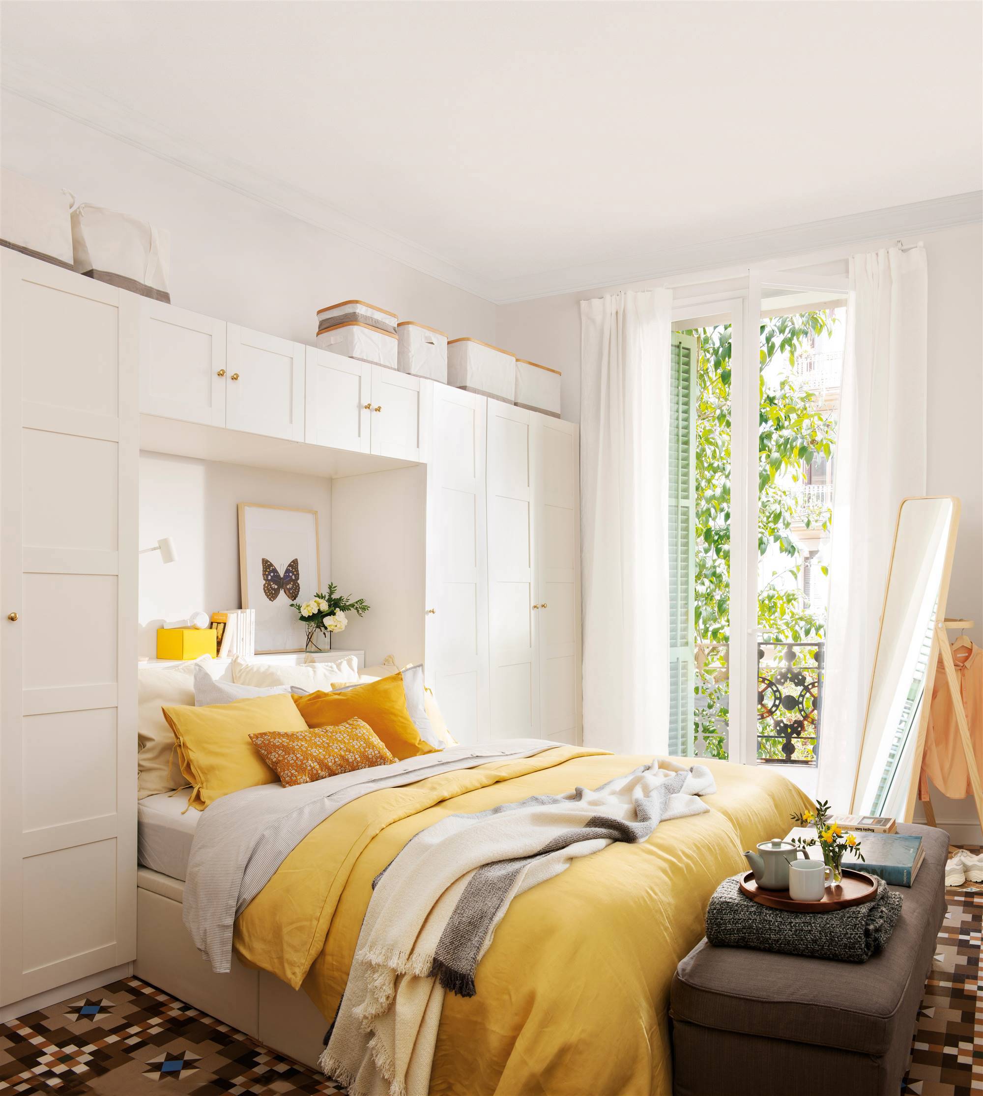 Dormitorio con armario tipo puente, banco con almacenaje y ropa de cama amarilla y blanca. 