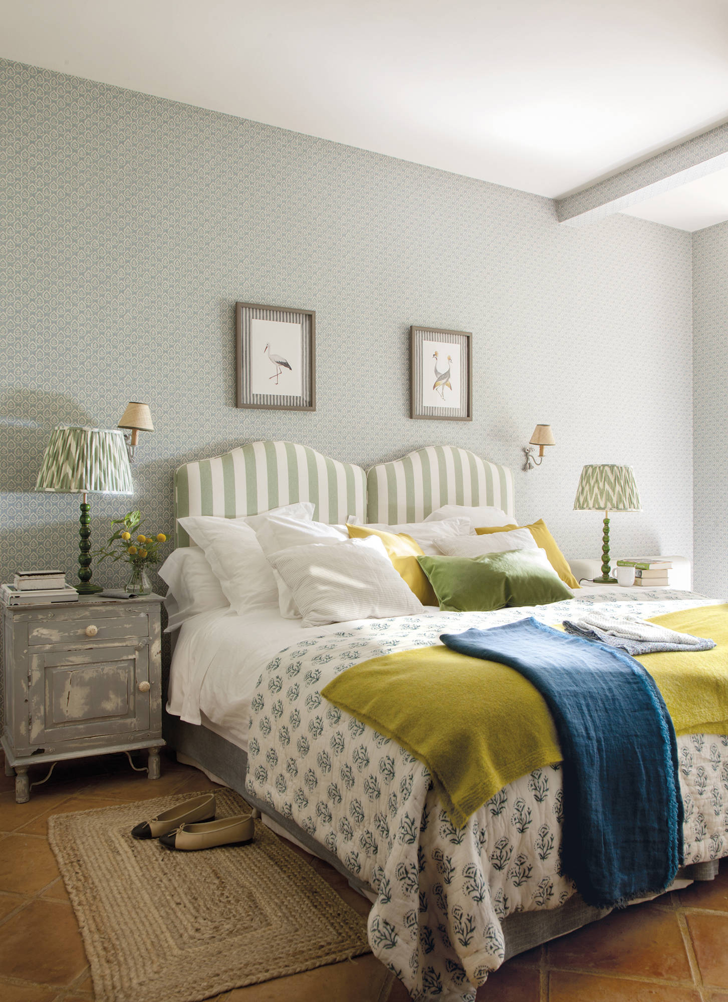 Dormitorio en verde con cabecero tapizado a rayas a medida, mesitas auxiliares envejecidas y alfombra de fibras.