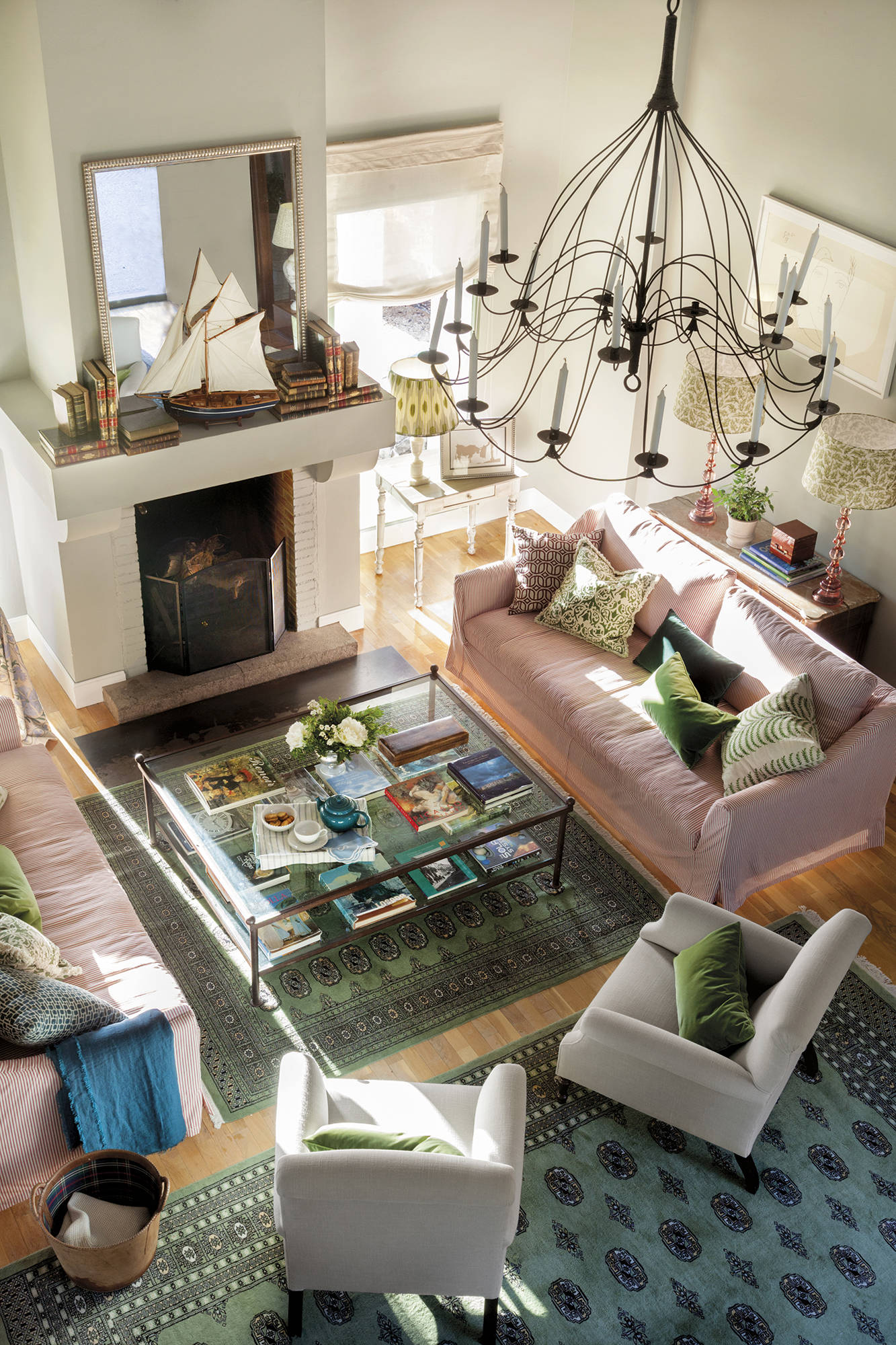 Salón con chimenea, lámpara de araña, alfombras, cojines con telas y sofás con fundas de rayas. 