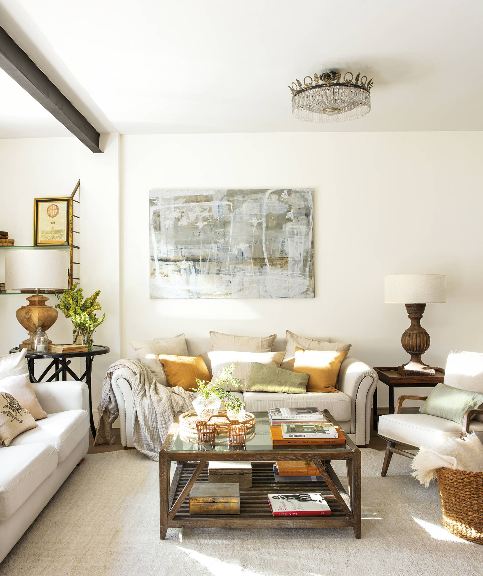 Salón blanco con sofás beige retapizados, mesa de centro de madera y lámina abstracta.