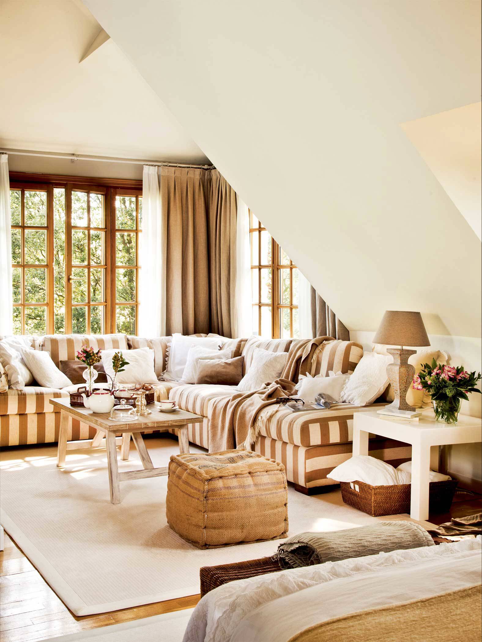 Salón con sofá rinconero con estampado a rayas bicolor y puff de fibra natural. 