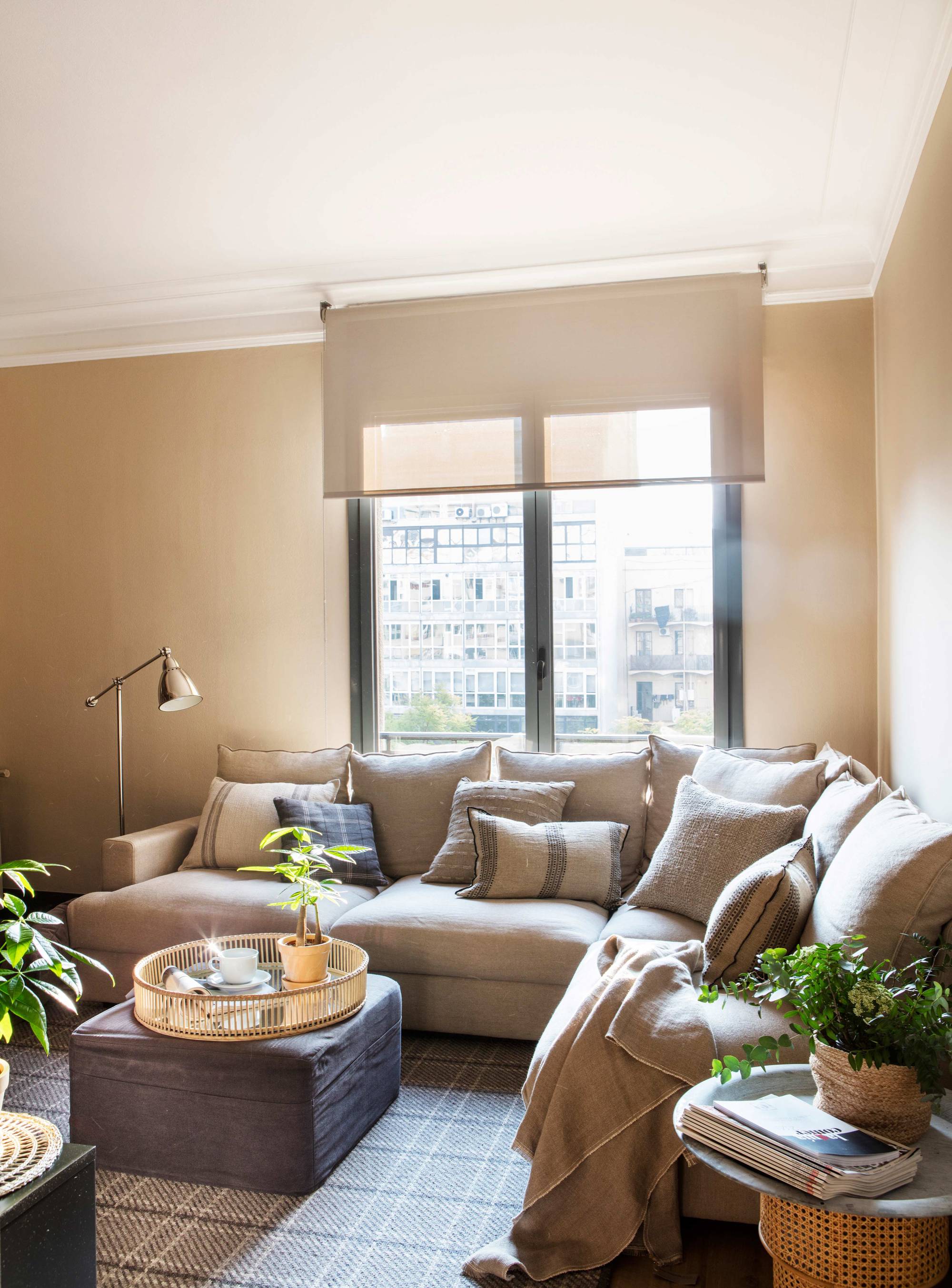 Salón con sofá rinconero en beige y alfombra de cuadros. 