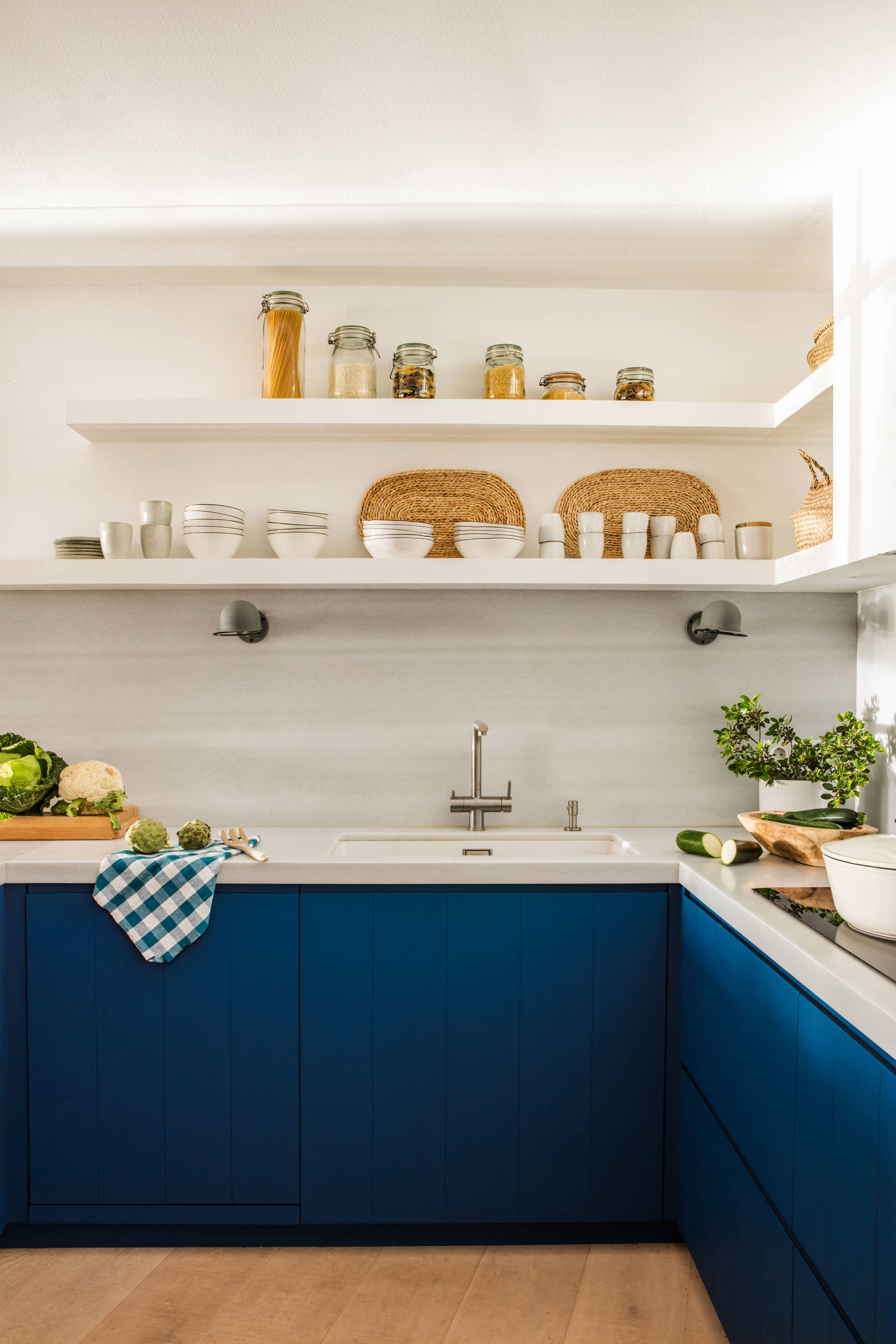 Cocina con mobiliario azul, encimera y estantes blancos.