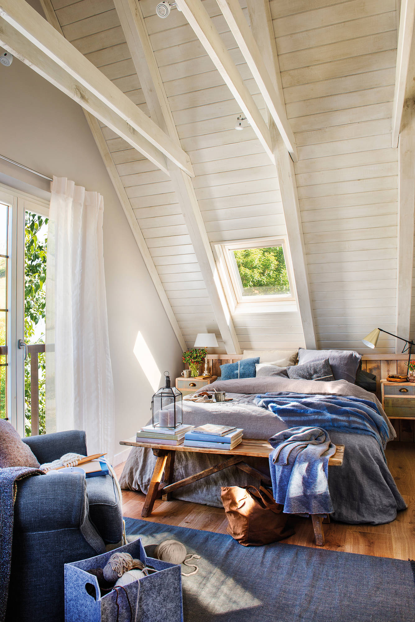 Dormitorio abuhardillado con paredes y techo blancos y ropa de cama azul. 
