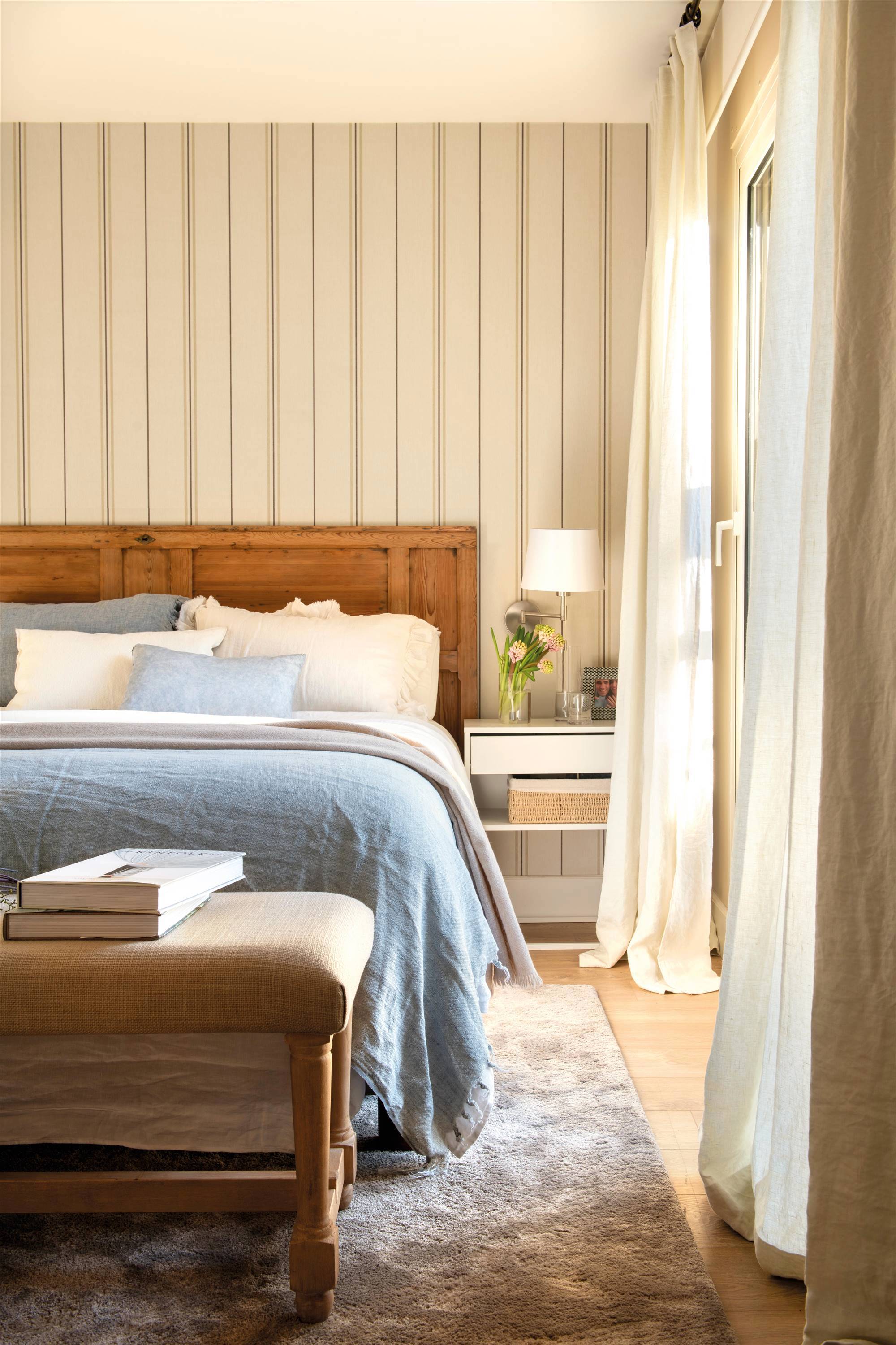 Dormitorio con cabecero de madera y papel pintado de rayas en la pared del cabecero. 