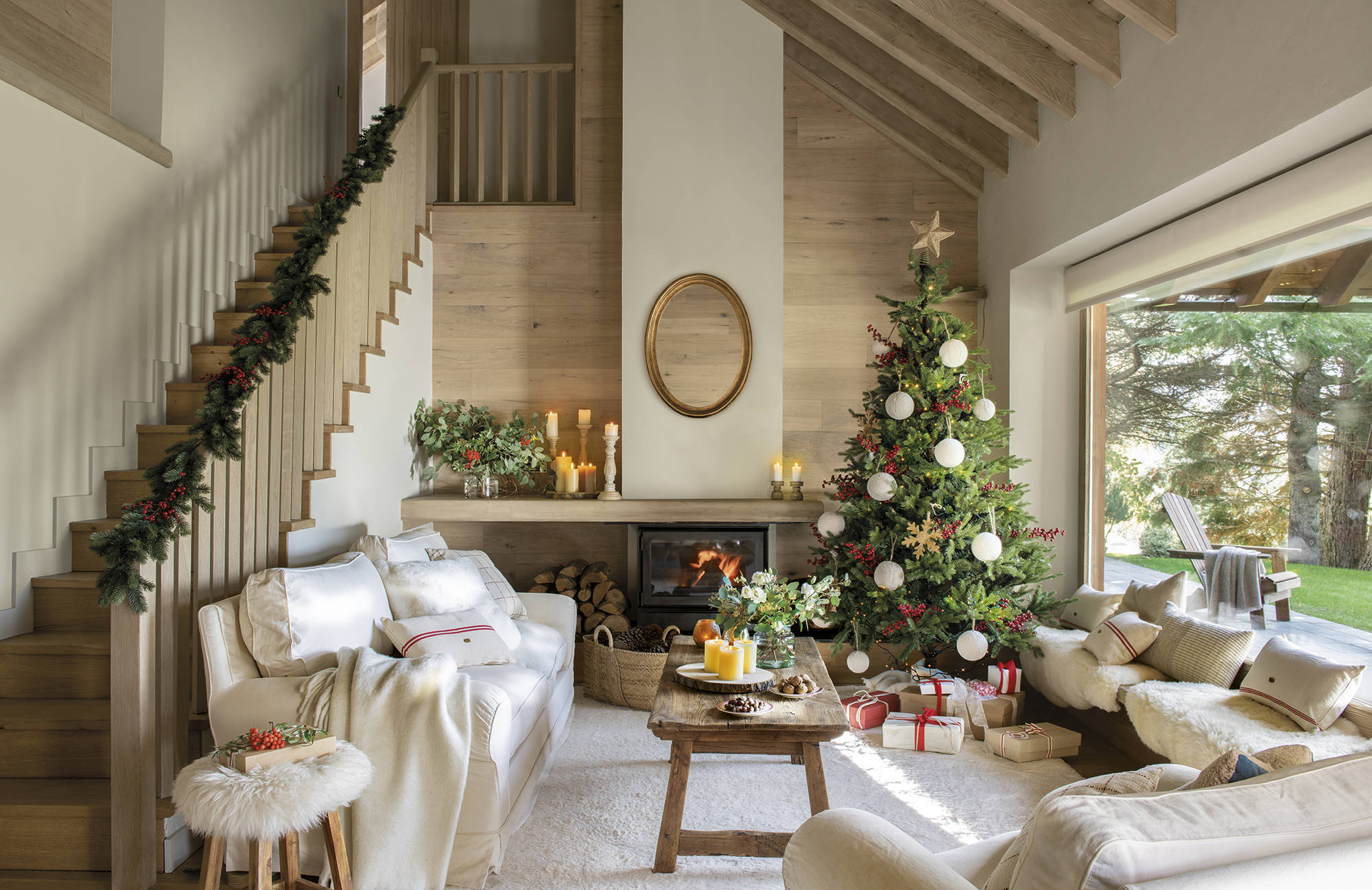 Salón rústico con escalera, árbol de Navidad, chimenea y sofás blancos.