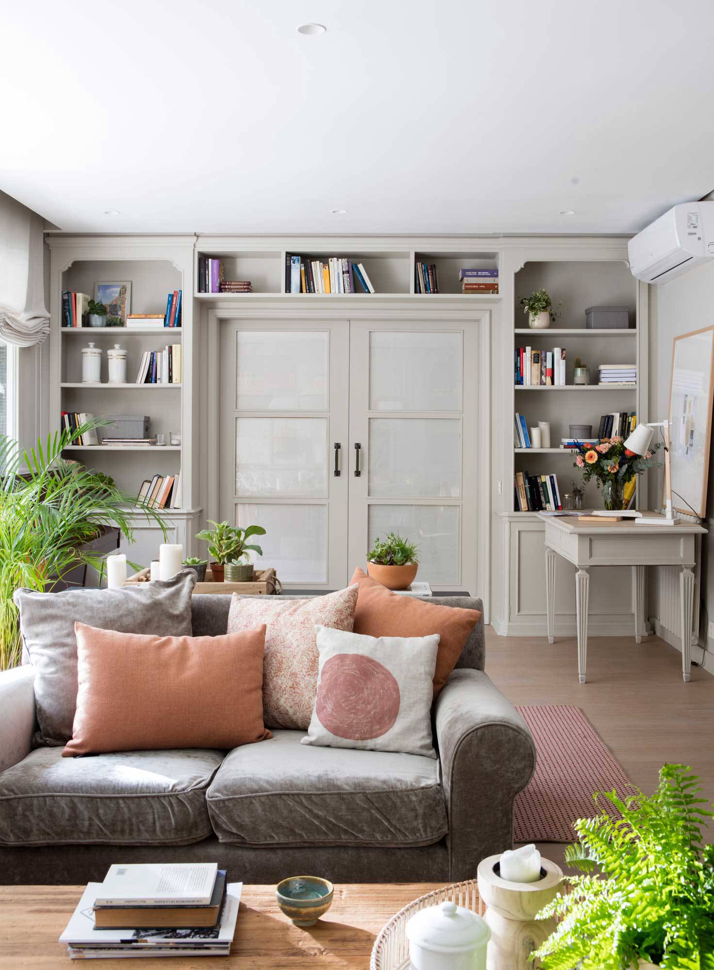 Salón con sofá gris, cojines y coral y librería