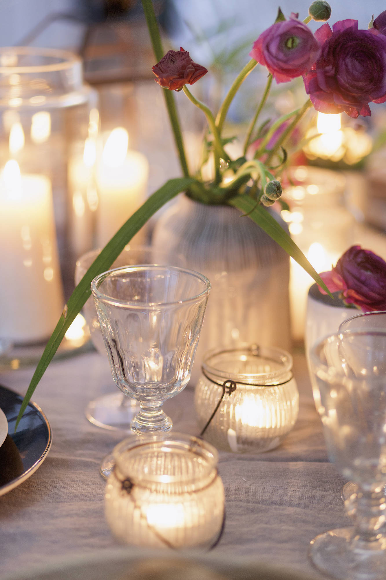 Mesa con velas encendidas, jarrón con flores y copas de cristal.