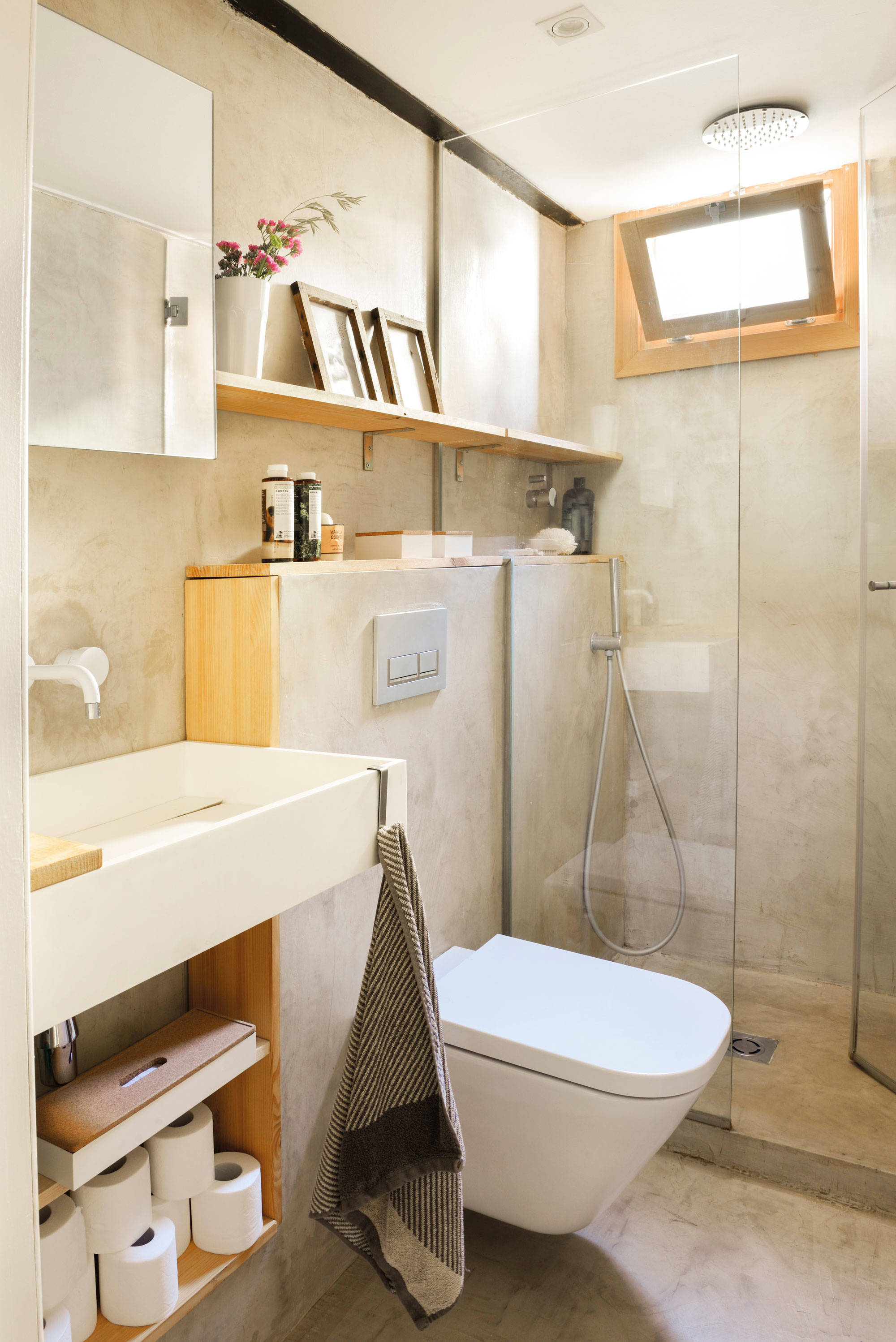 Baño con ducha y estantería de obra y estante de madera sobre el inodoro.