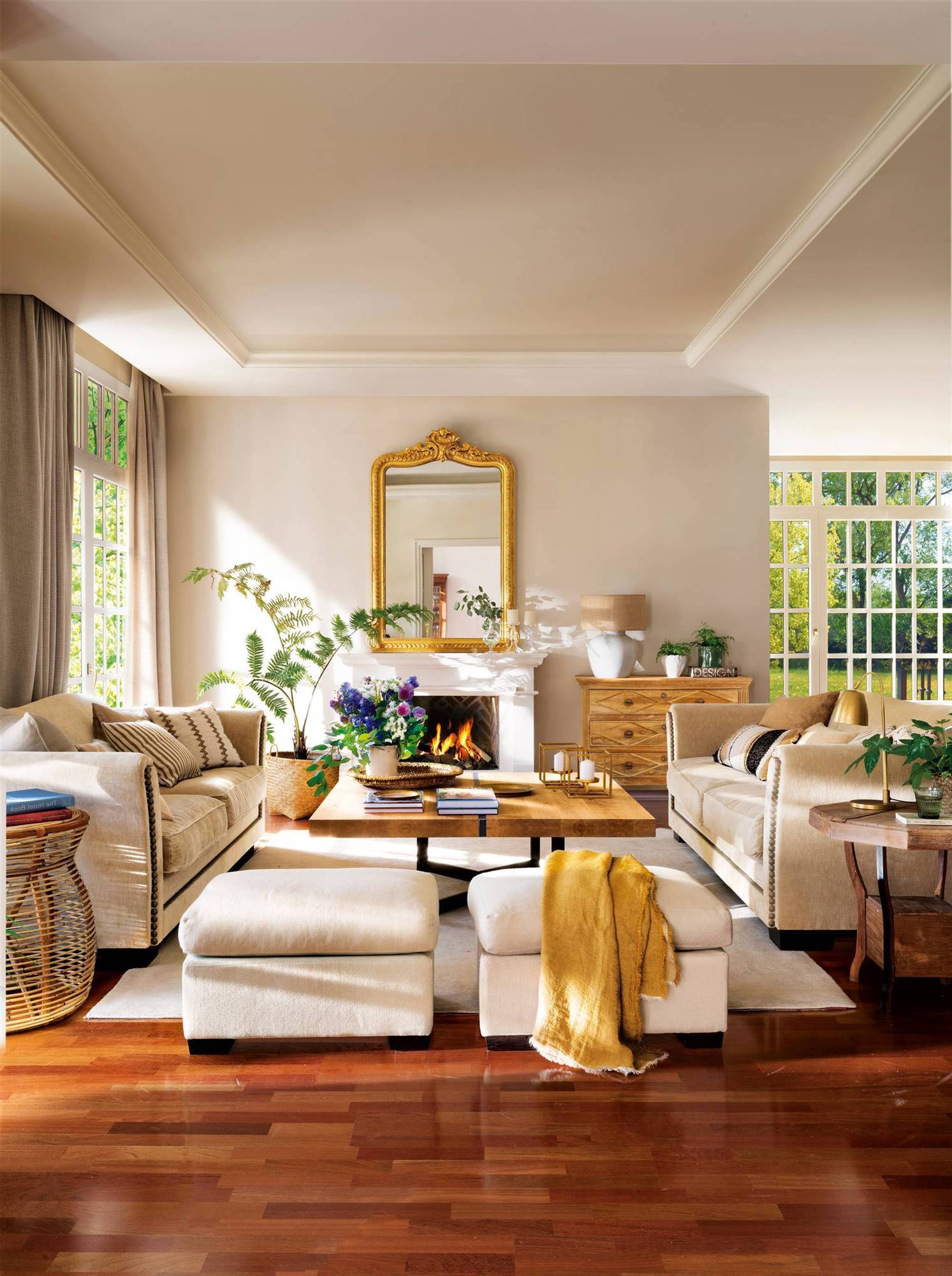 Salón con chimenea y espejo dorado, sofás blancos y suelo de madera oscuro.