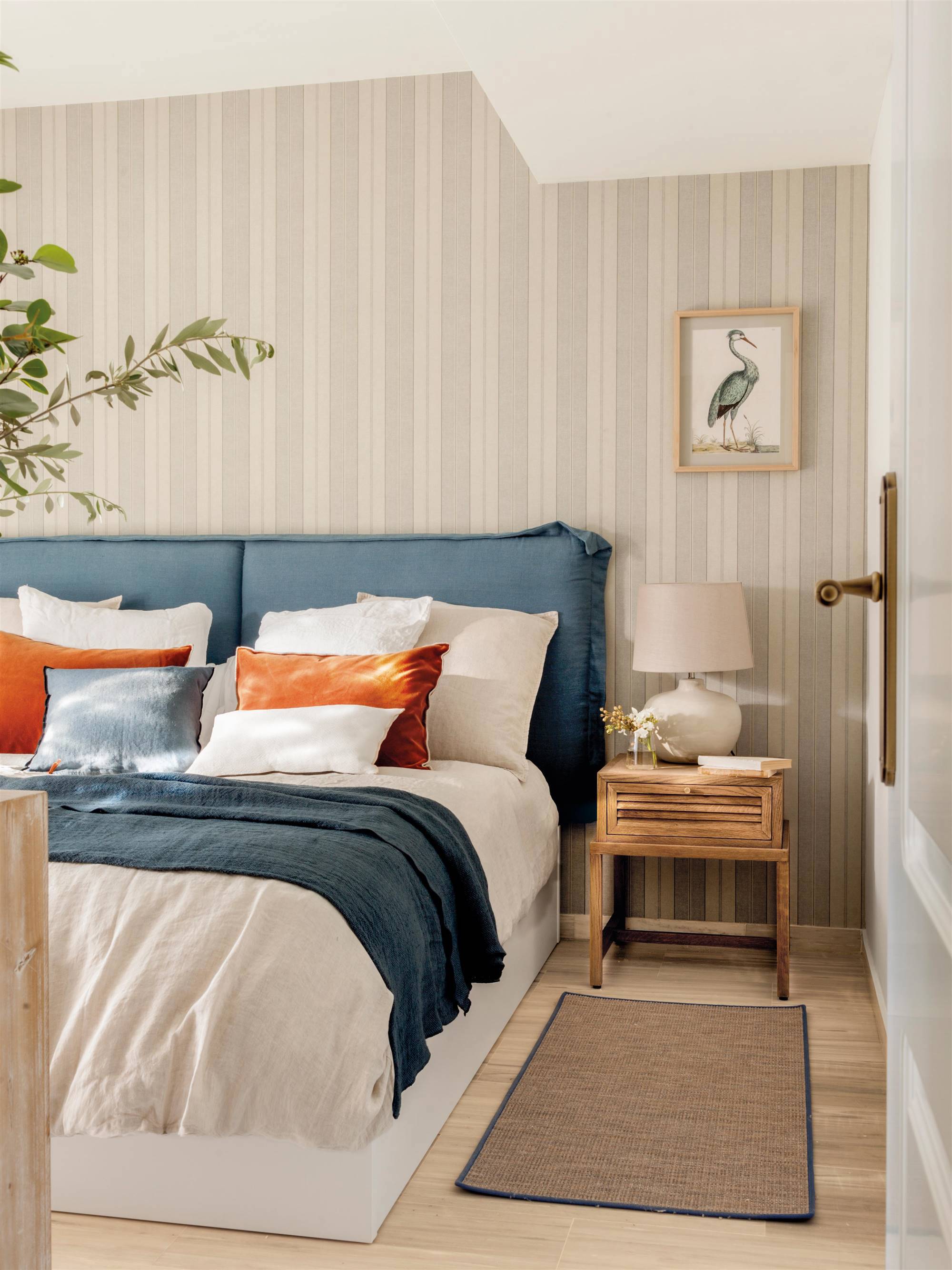 Dormitorio de primavera con cabecero tapizado en azul y papel pintado de rayas.