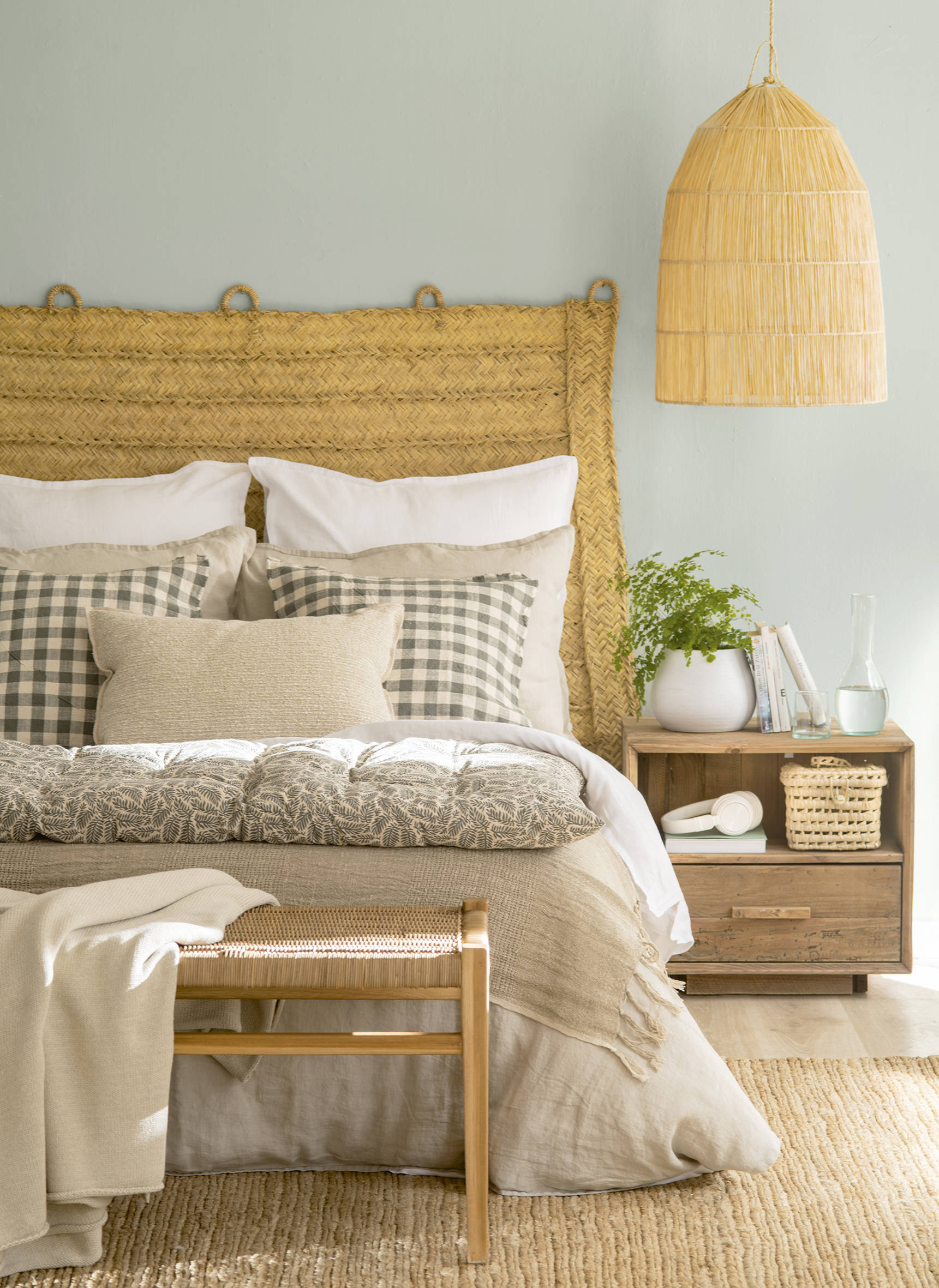  Dormitorio con cabecero de esparto, mesilla de madera sin tratar y ropa de cama beige y verde.558438