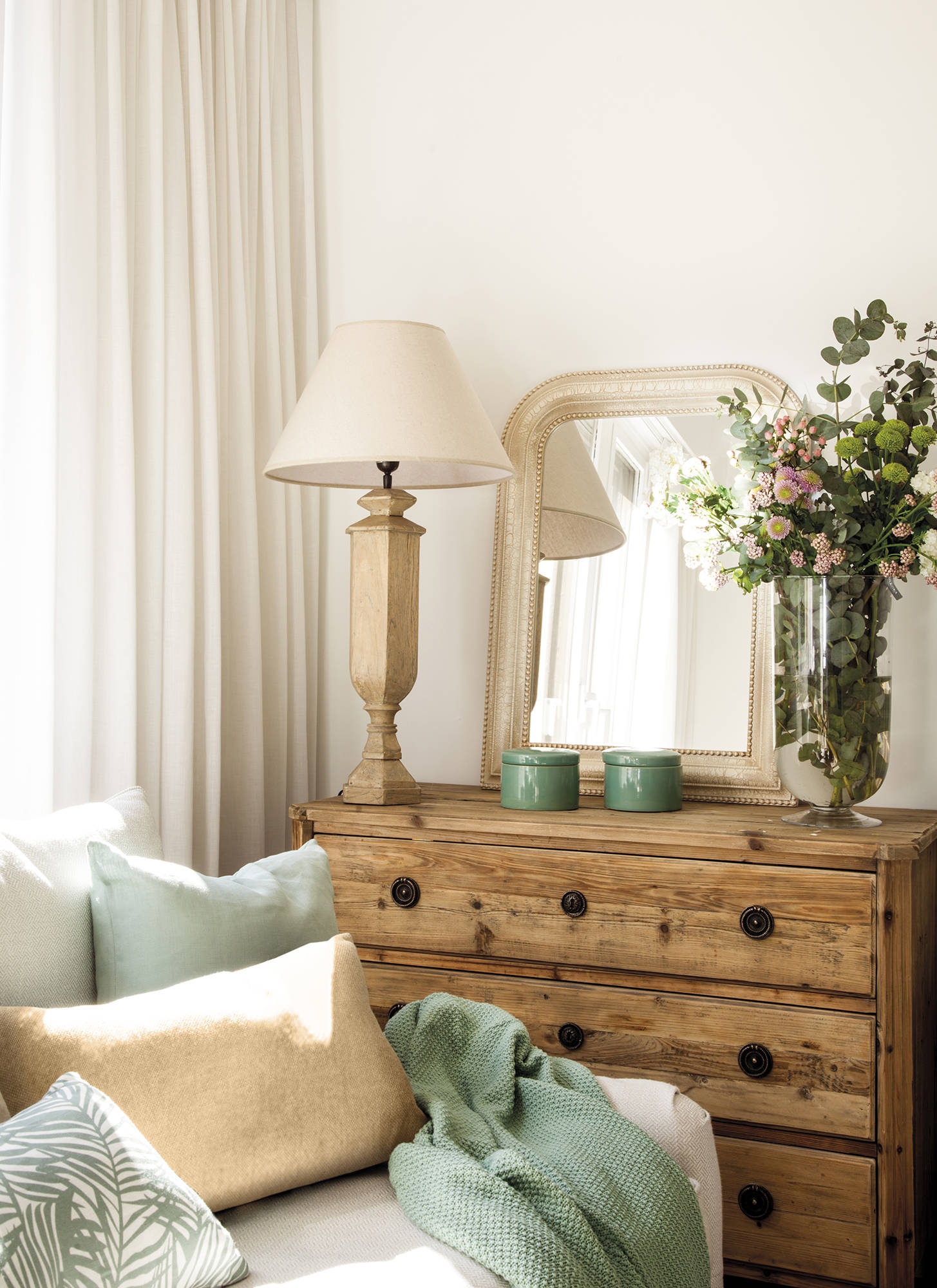 Salón con sofá blanco y cómoda de madera decorada con lámpara de sobremesa y espejo.