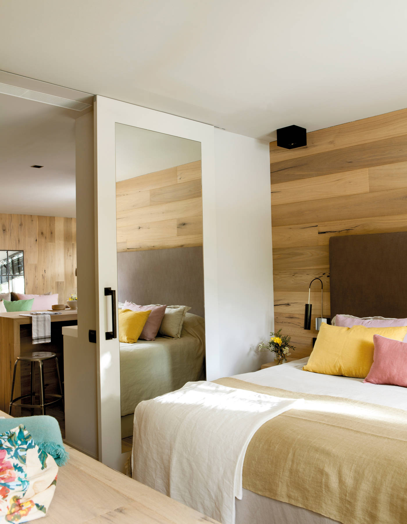 Dormitorio con puerta corredera con espejo y pared forrada de madera