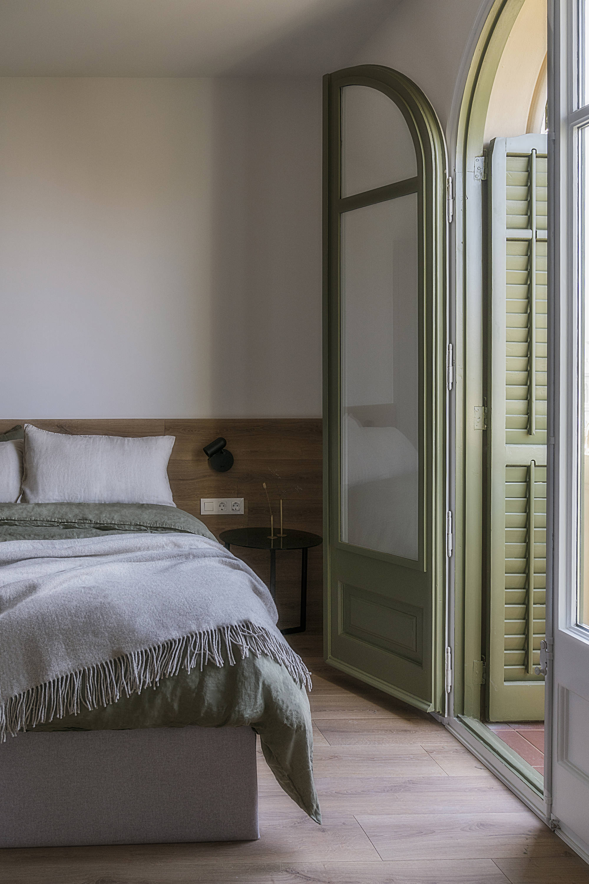 Dormitorio después de la reforma con ventana verde, cabecero de amdera y cama con canapé gris abatible
