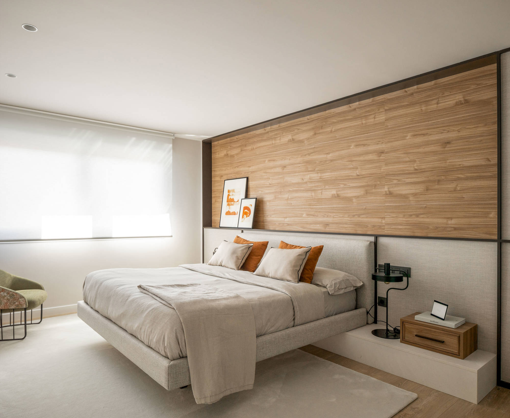 Dormitorio principal moderno con cabecero de madera y tapizado, cama voladiza, alfombra y butaca verde. 