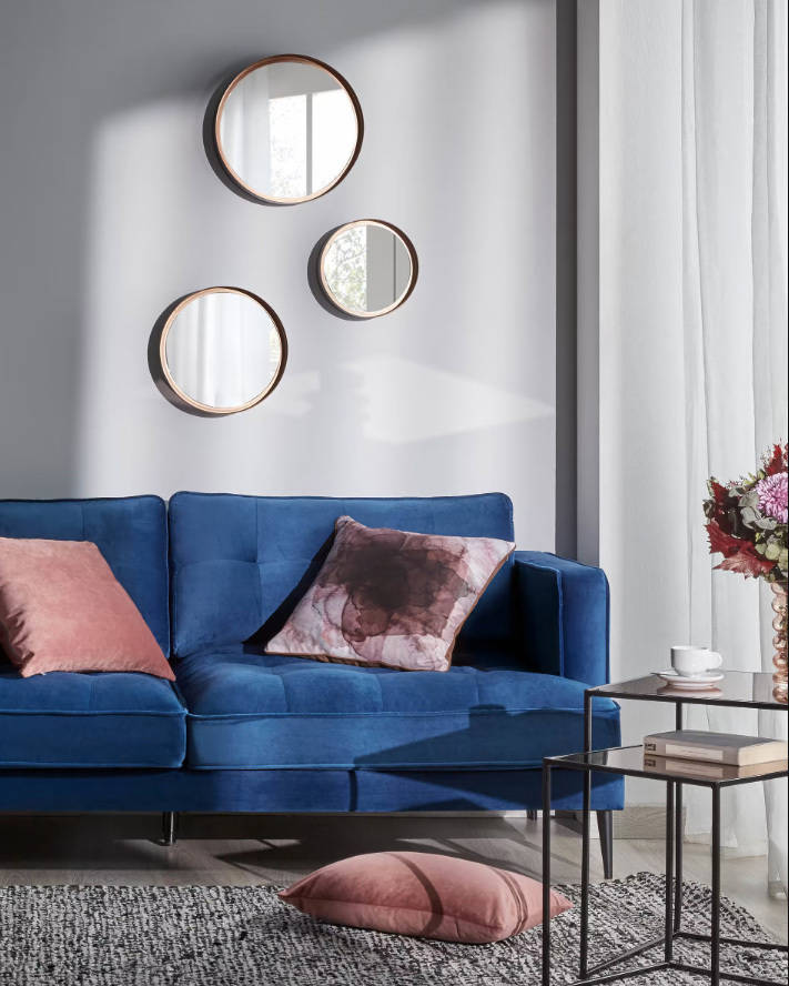 Salón con sofá azul y tres espejos redondos de diferentes tamaños con marco de madera