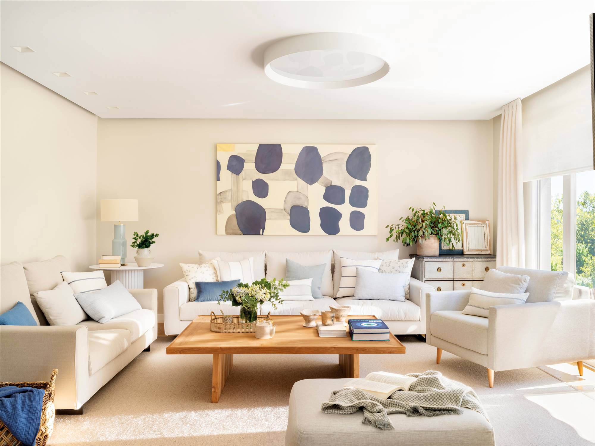Salón de primavera con sofás en blanco, butaca gris y cuadro con pinceladas azules.