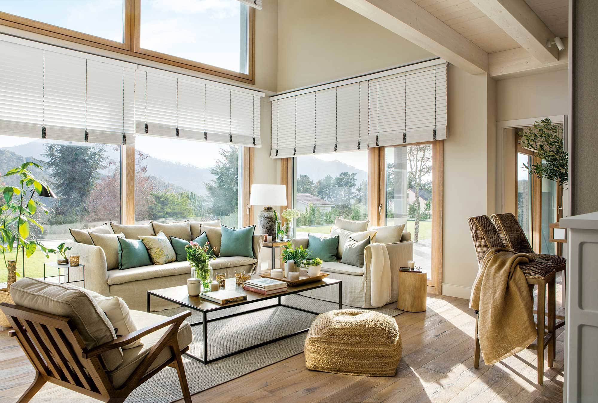 Salo´n con grandes ventanales, sofá de lino y cojines en blanco y verde.