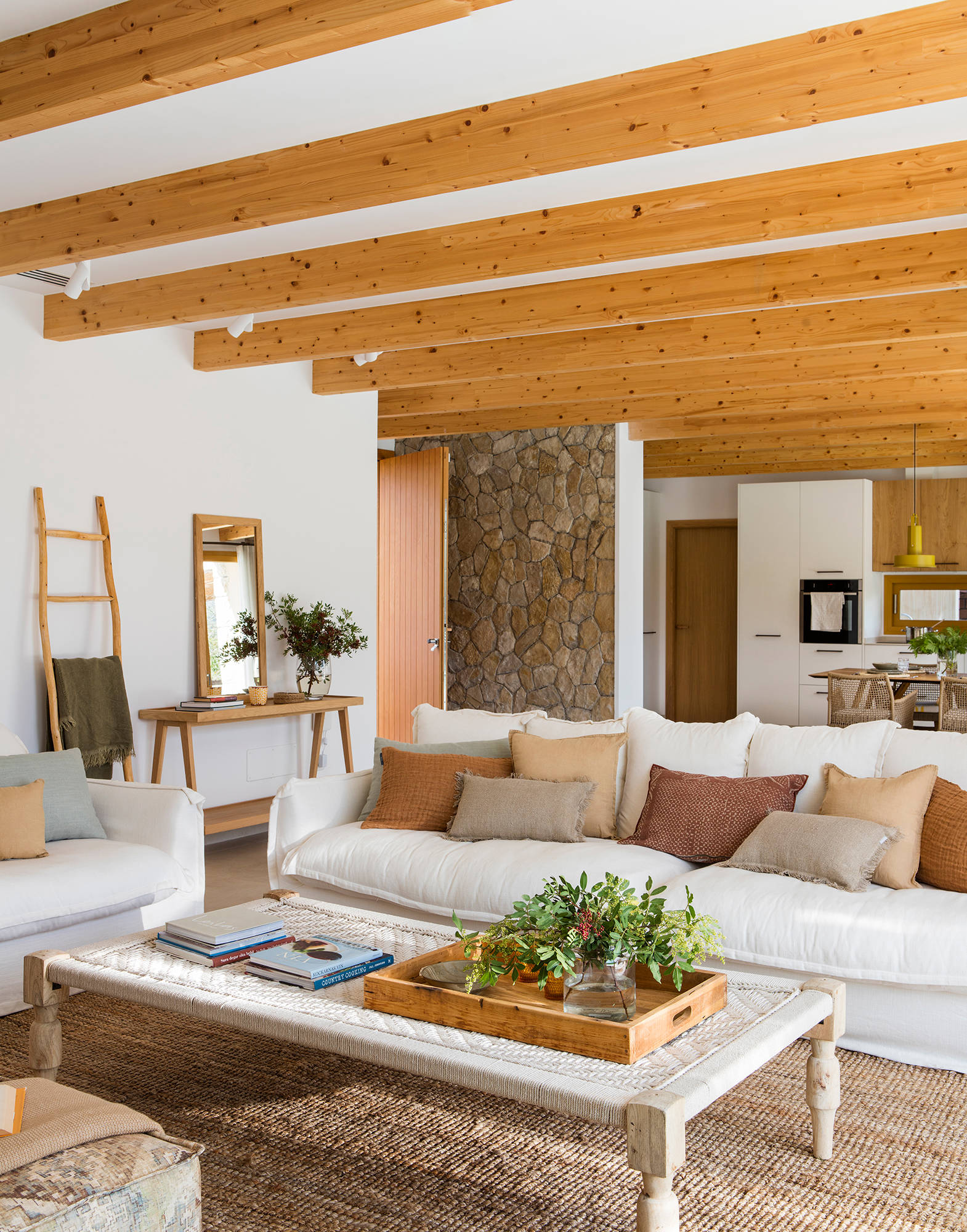 Salón con sofá blanco, vigas de madera en techo y cojines en colores tierra..