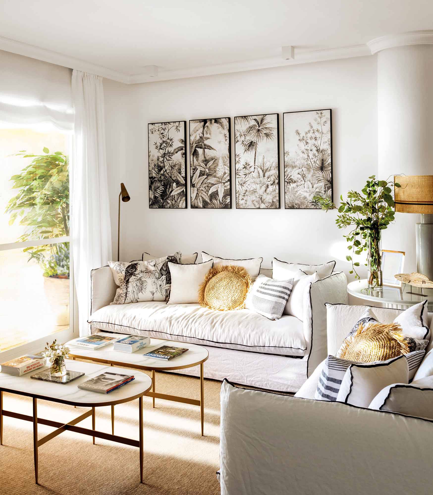 Salón con sofá blanco con ribete negro, mesas de centro doradas y ovaladas y cuadros de palmeras