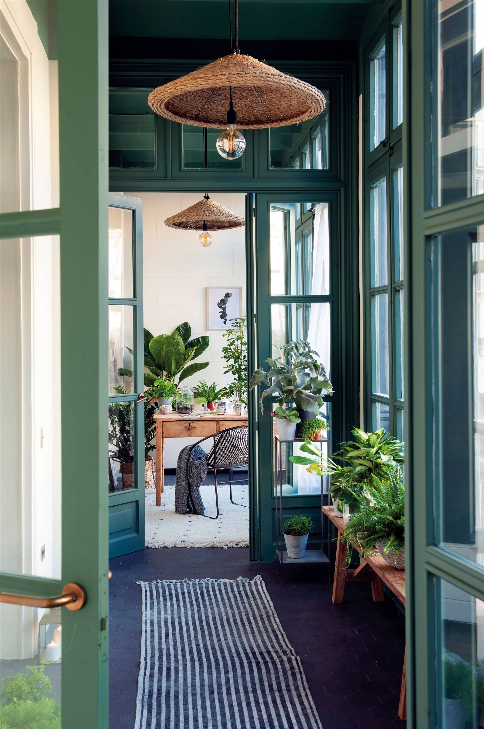 Galería con plantas, lámparas de fibra y puertas pintadas de verde.