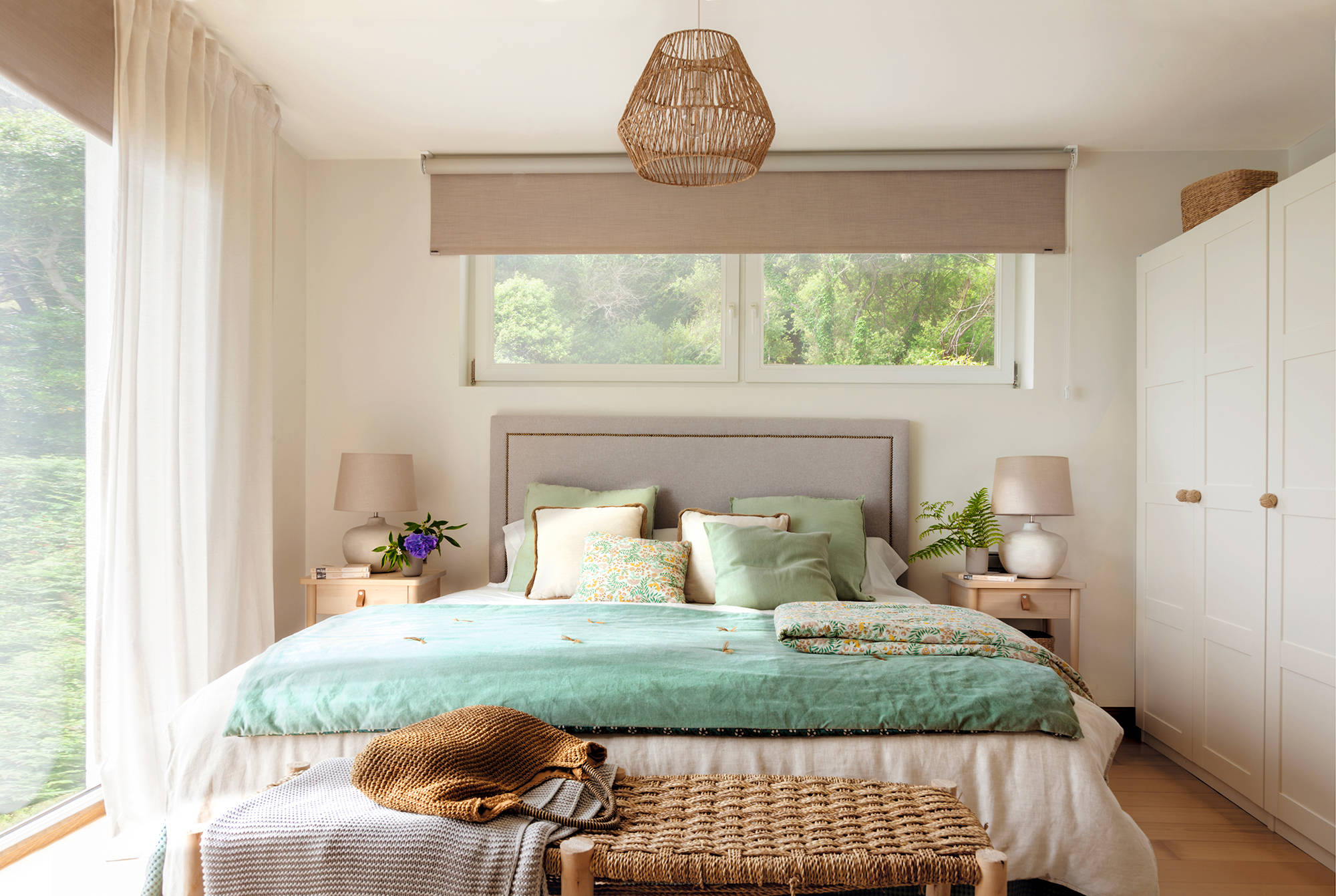 Cama debajo de la ventana con cabecero tapizado en gris y ropa de cama en turquesa.