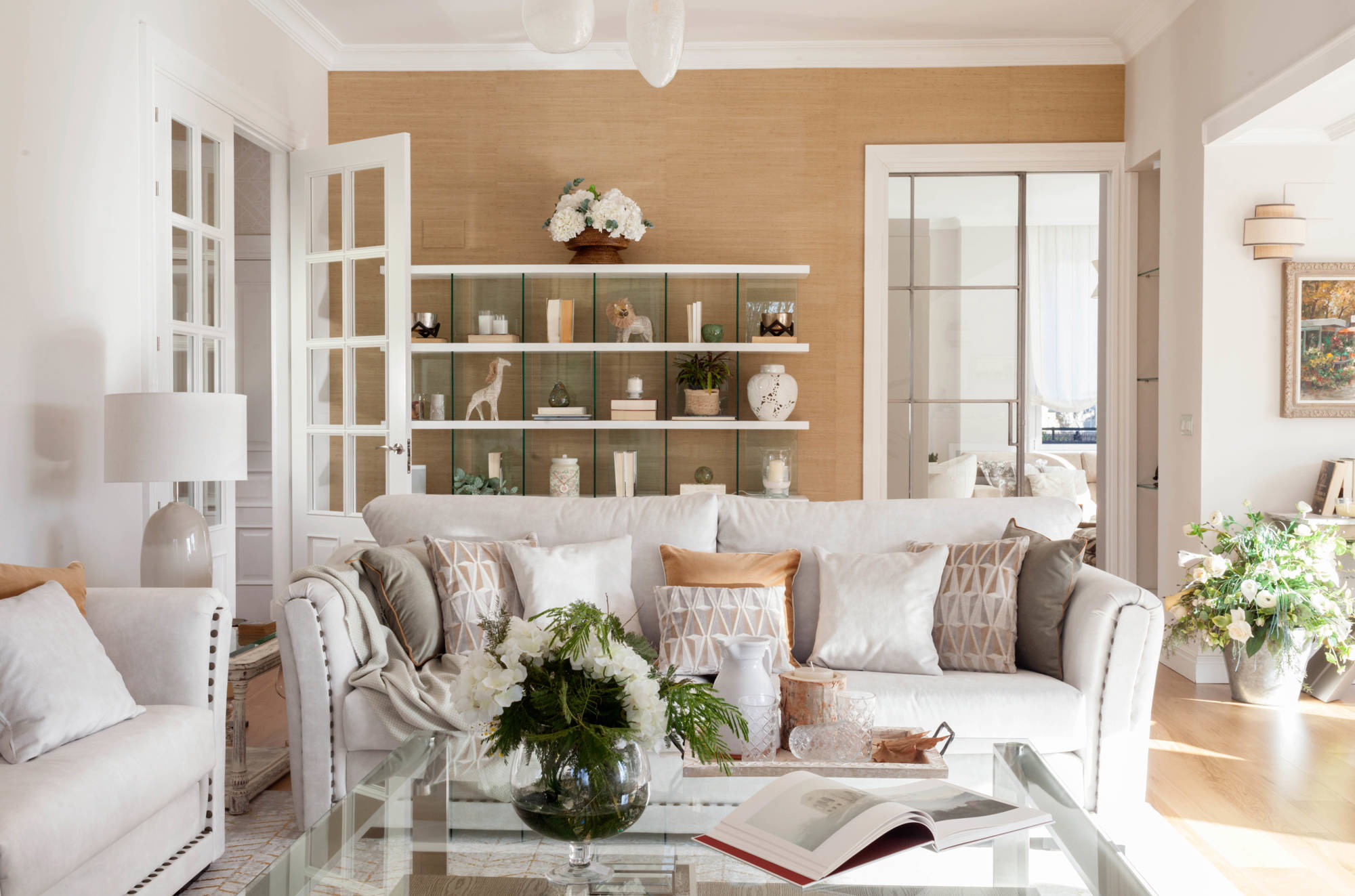 Salón con sofás blancos tapizados, estantería detrás y pared ocre. 