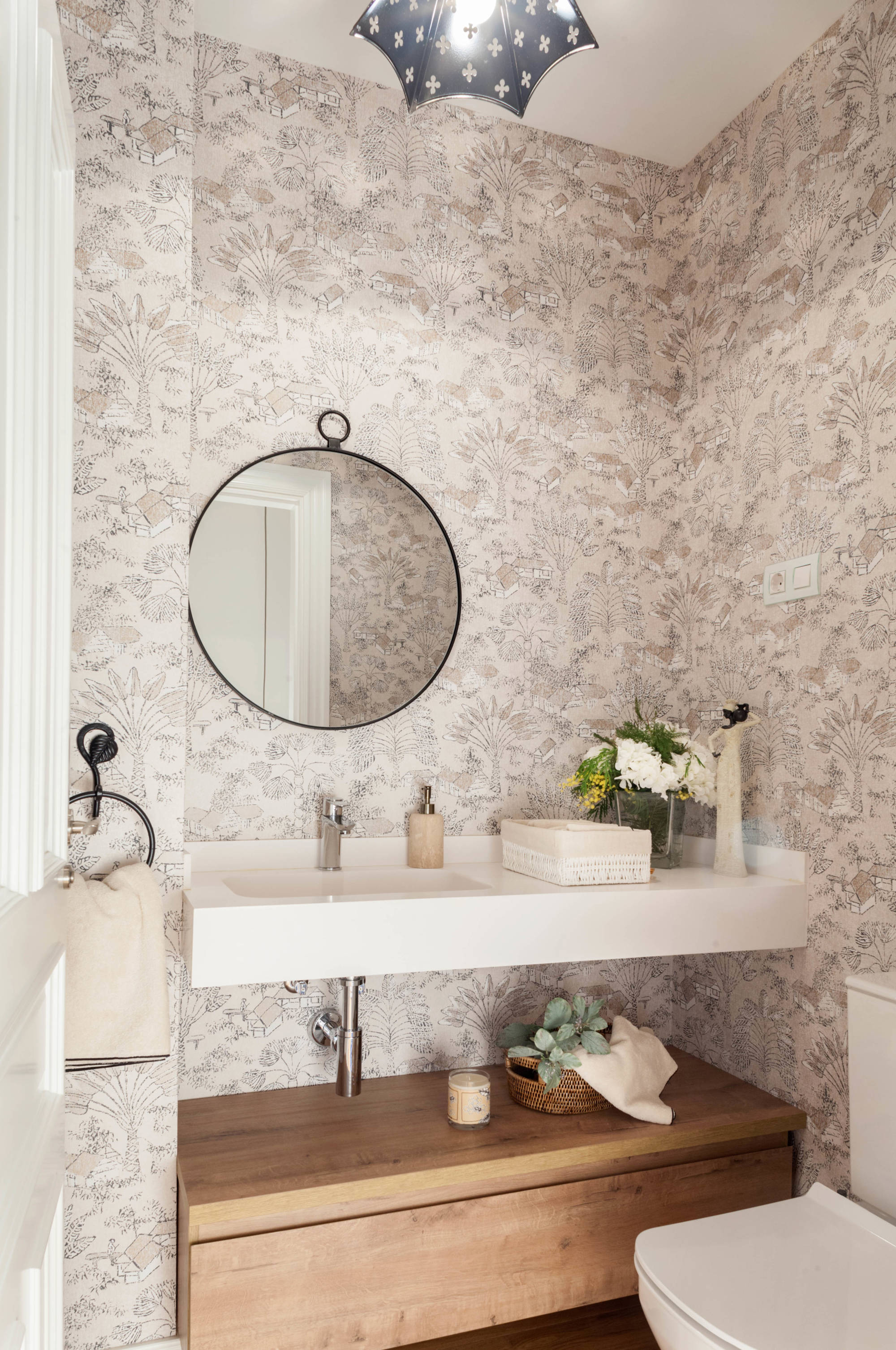 Baño pequeño con papel pintado con mueble hecho a medida y espejo redondo.